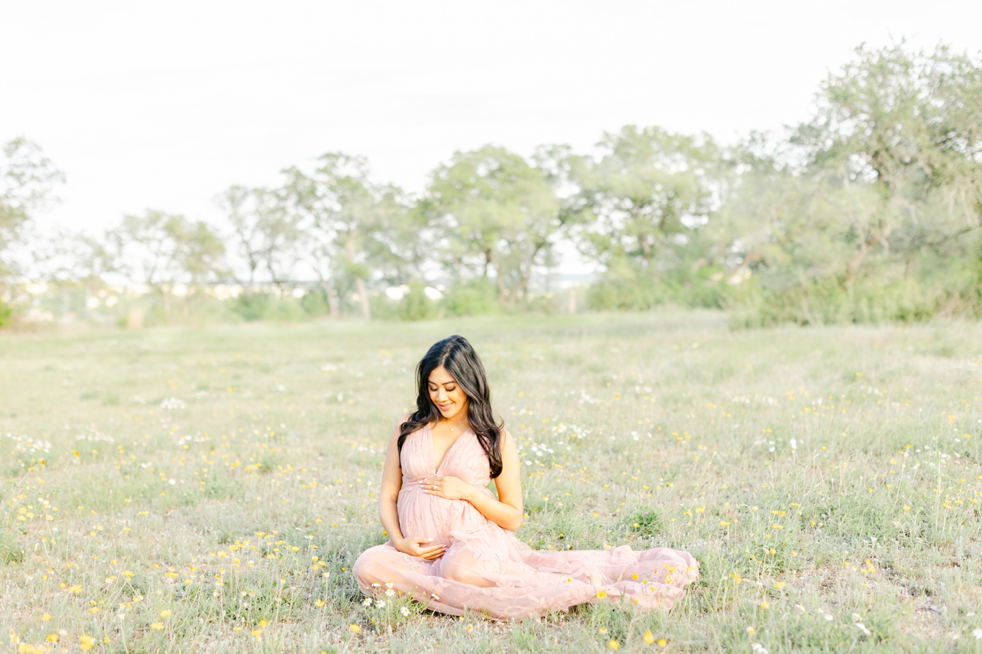 Expecting Mama sitting in wildflowers during maternity photoshoot outside of Round Rock, TX. Photo by Sana Ahmed Photography.