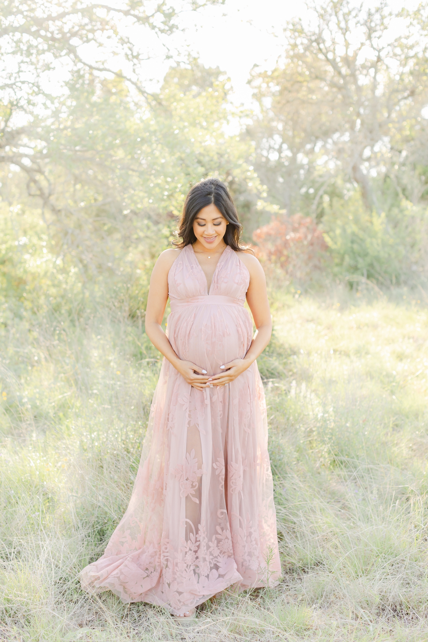Pregnant Mom in pink lace maxi dress looking at bump during field maternity session with Sana Ahmed Photography.
