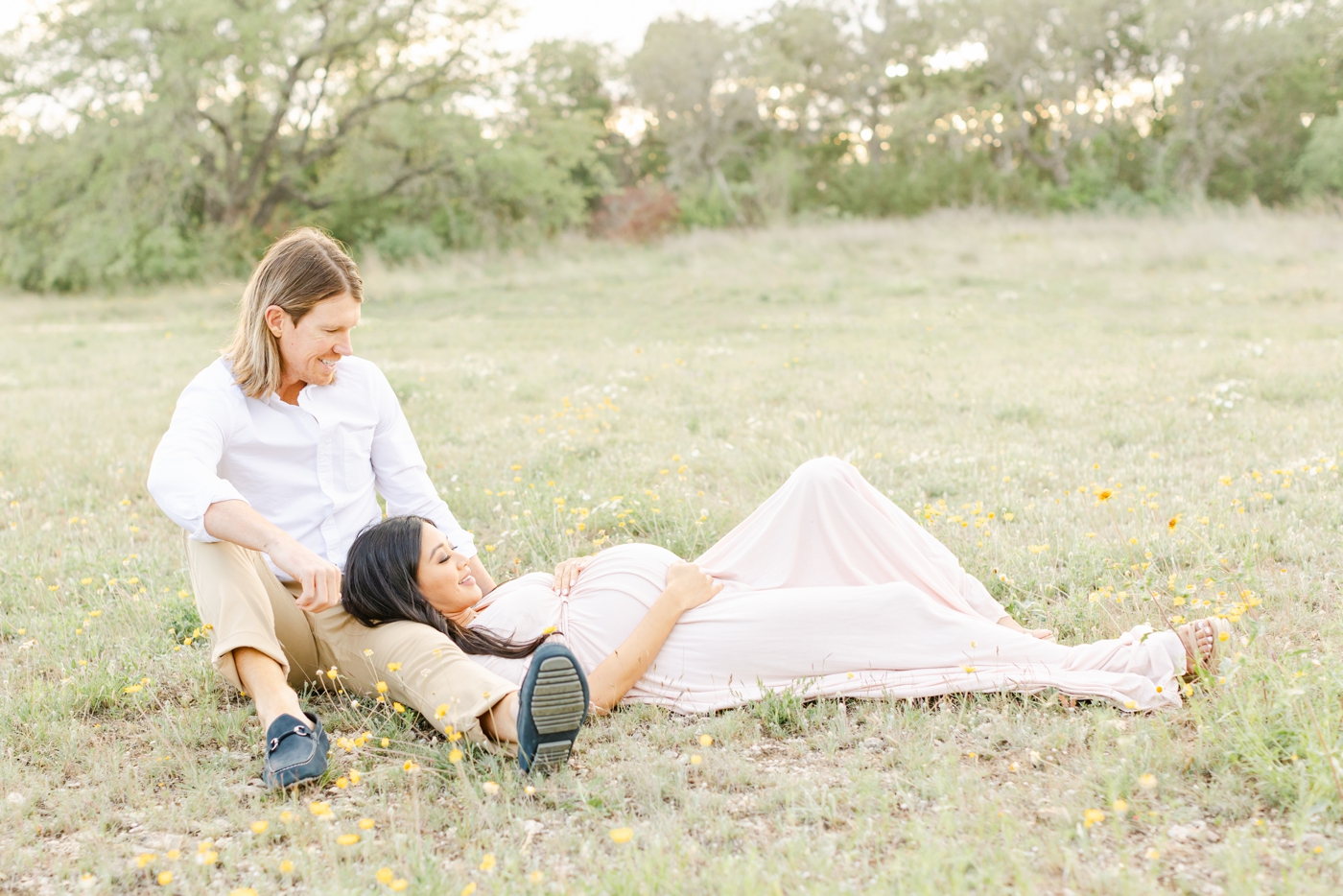 Expectant parents sitting in wildflowers during maternity photoshoot by Round Rock photographer, Sana Ahmed Photography.