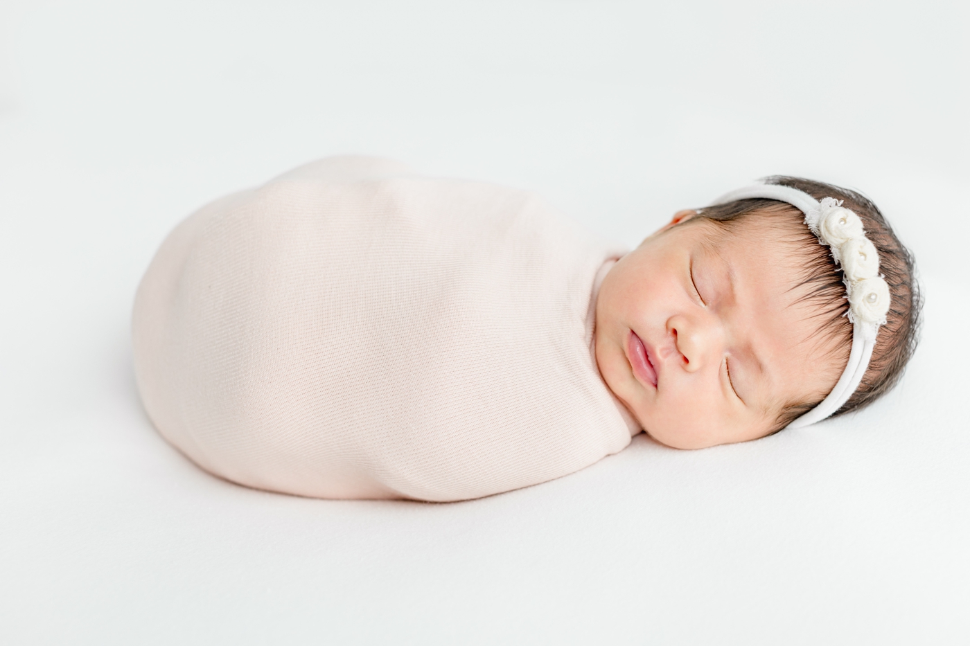 Sleeping baby in blush pink swaddle with white headband. Photo by Sana Ahmed Photography.