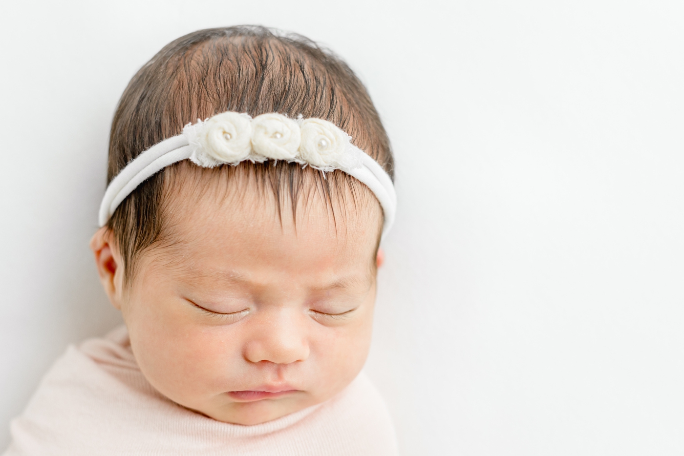 Newborn baby with dark hair and white headband sleeping during posed newborn session in Austin, TX studio. Photo by Sana Ahmed Photography.