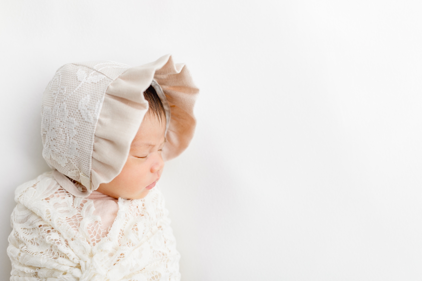 Baby wearing lace bonnet during light and airy studio newborn session with Sana Ahmed Photography.
