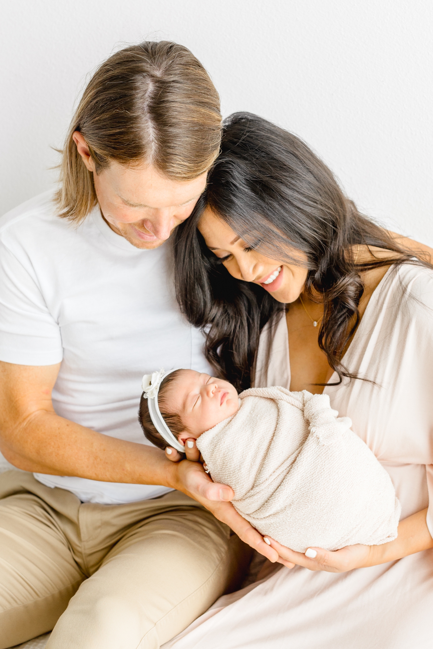 Mom and Dad cuddling and smiling at baby during light and airy studio newborn session with Sana Ahmed Photography.