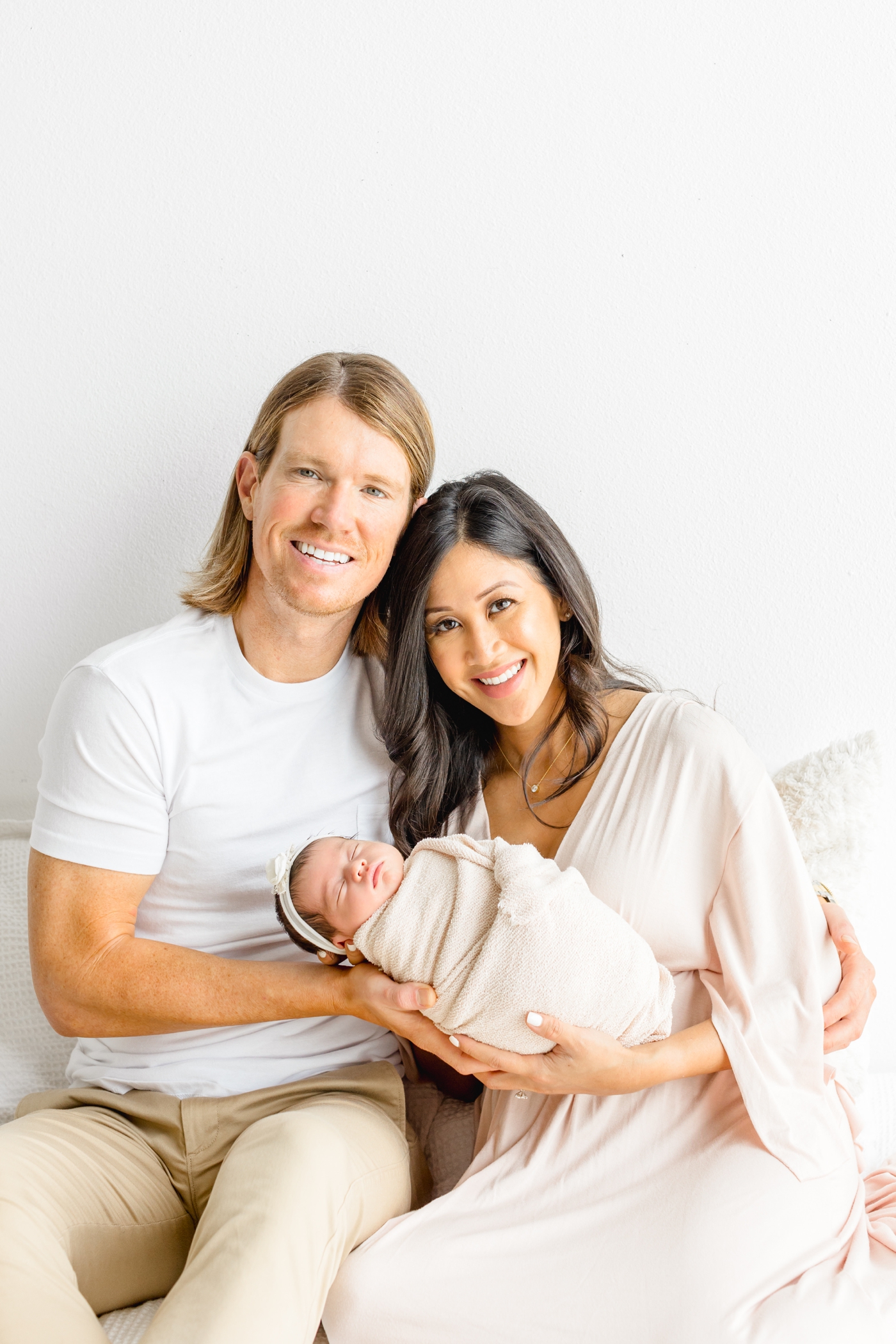Parents smiling at camera while they hold newborn during studio session. Photo by Sana Ahmed Photography.