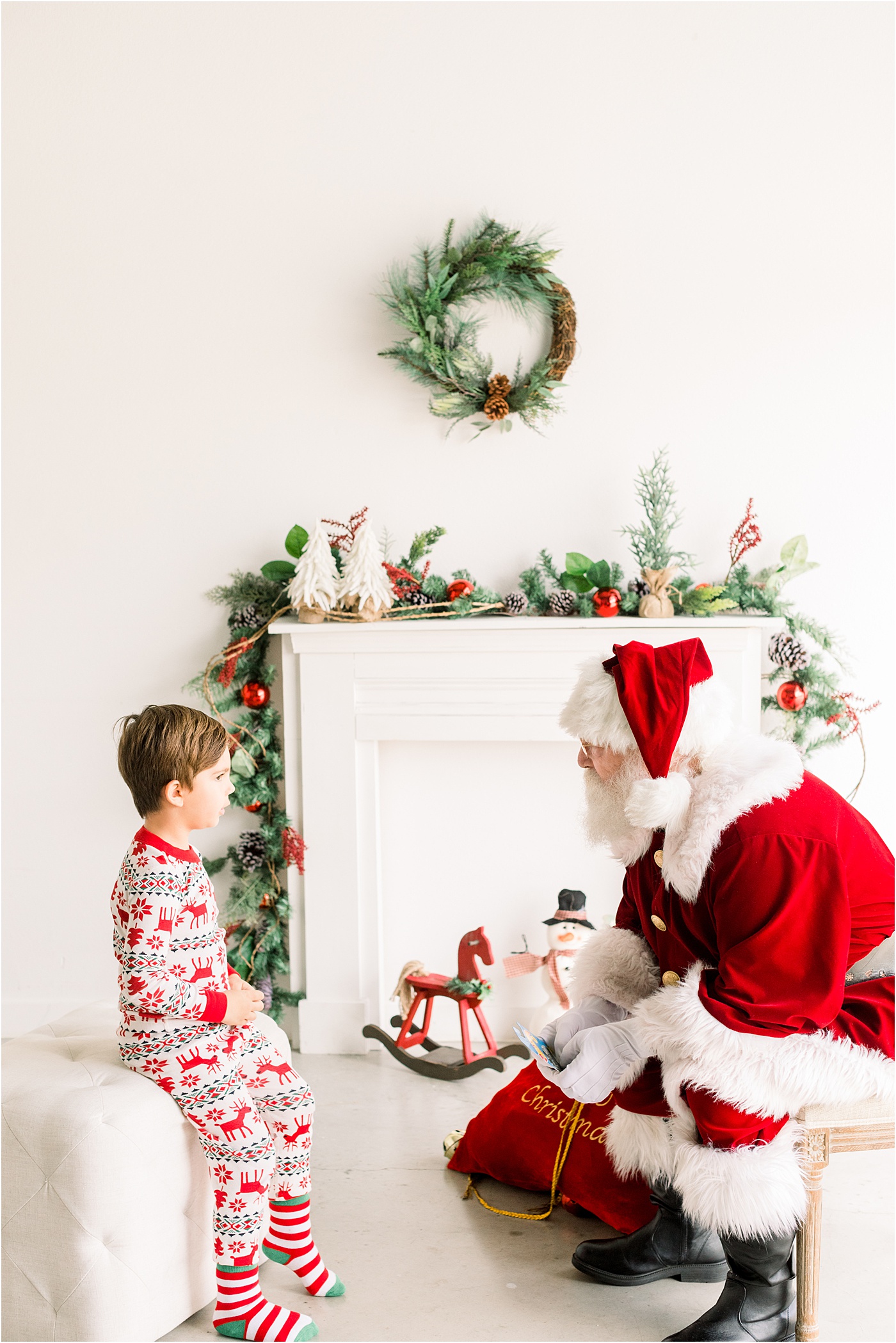 Santa talking with little boy who is wearing Christmas pajamas during mini session event with Sana Ahmed Photography.
