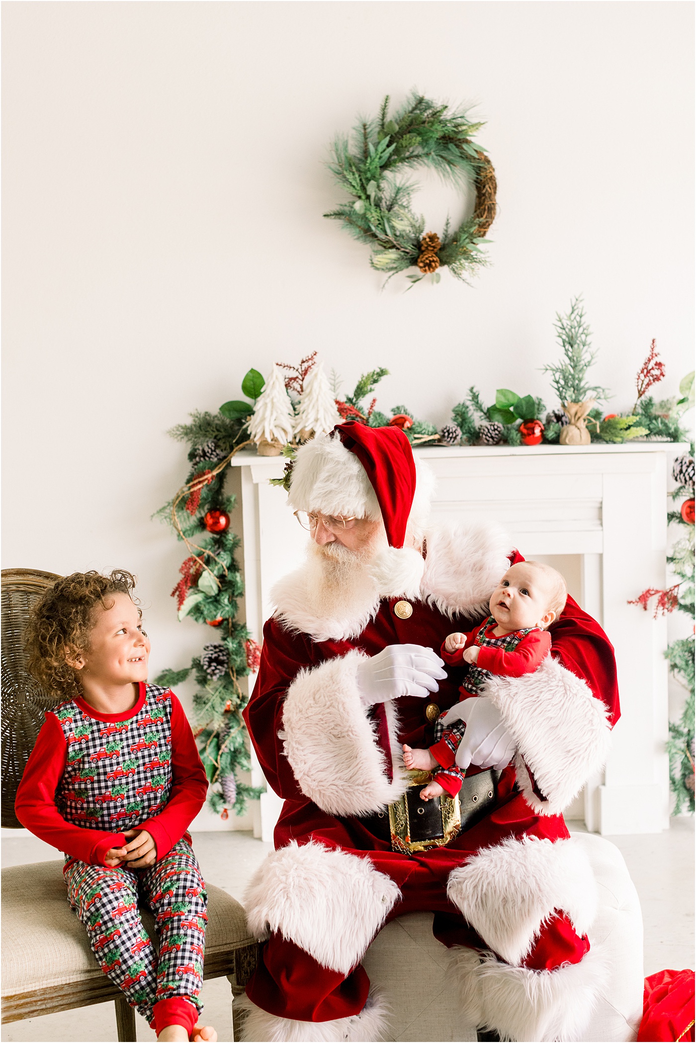 Image of Santa holding baby while talking with toddler next to him. Photo by Sana Ahmed Photography.