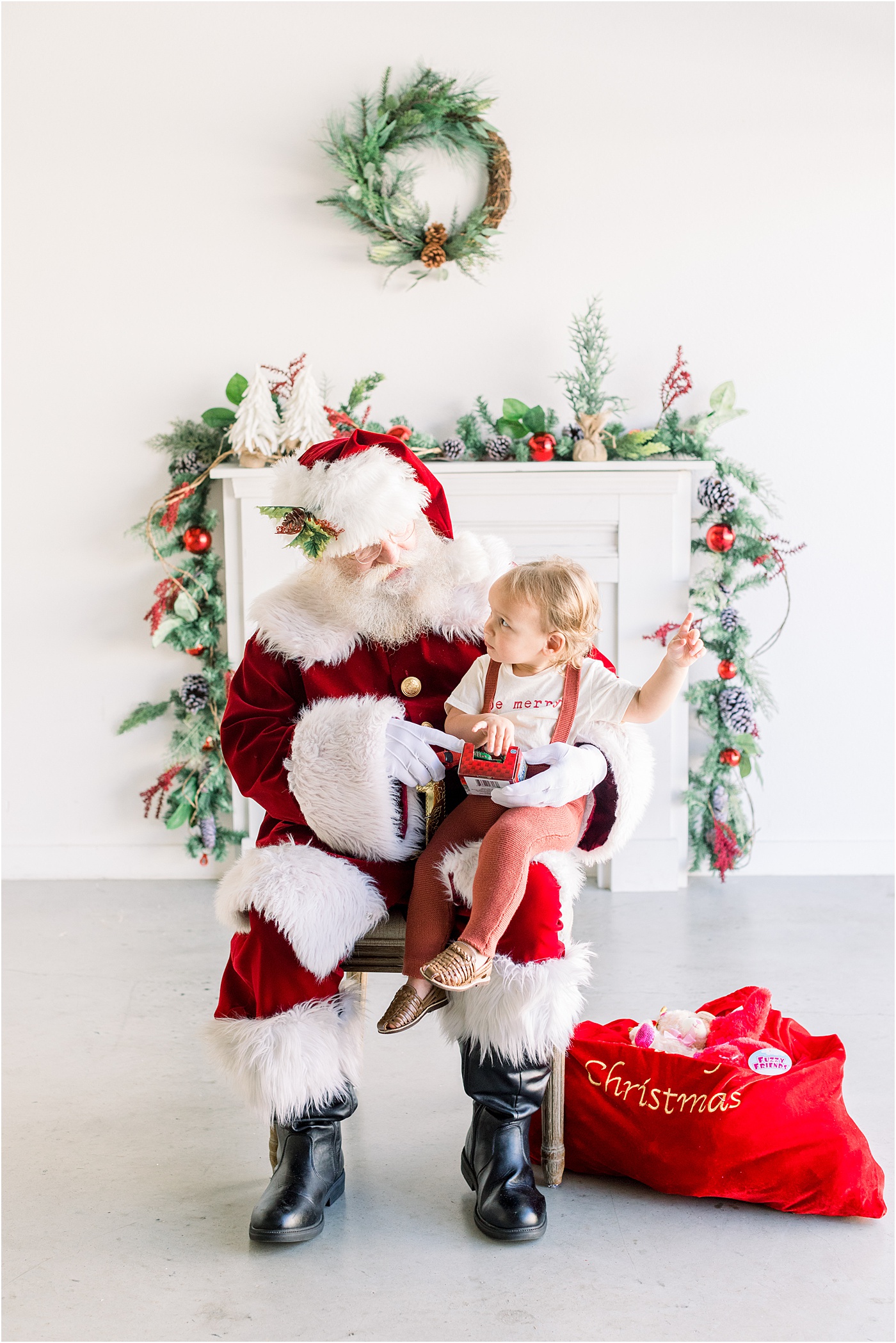 Little girl sitting on Santa's lap with a toy in her hand during mini session event with Sana Ahmed Photography.