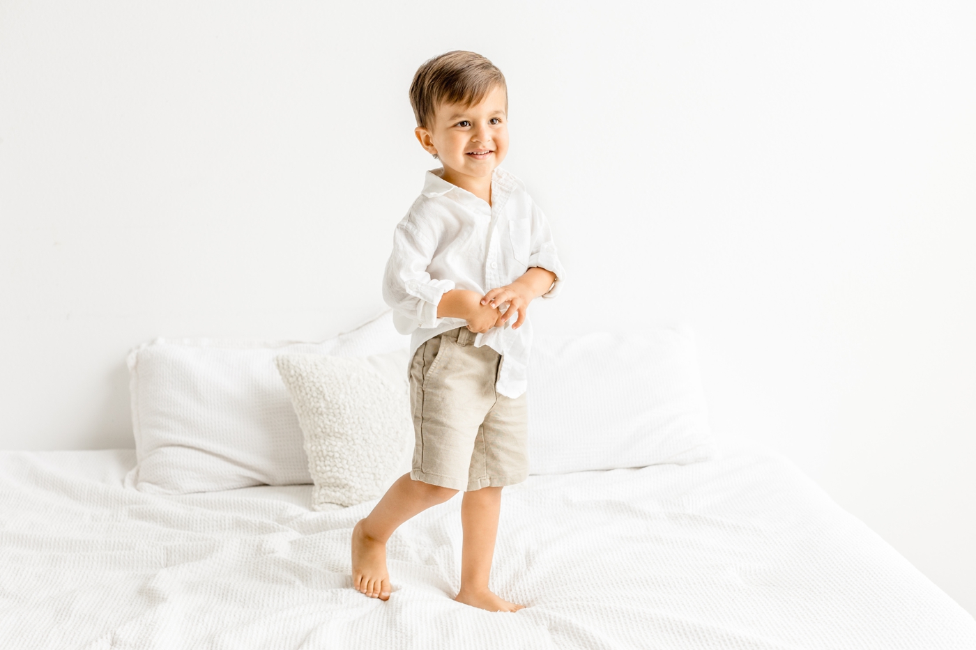 Little boy smiling on bed in Austin, TX studio. Photo by full service family photographer, Sana Ahmed Photography.