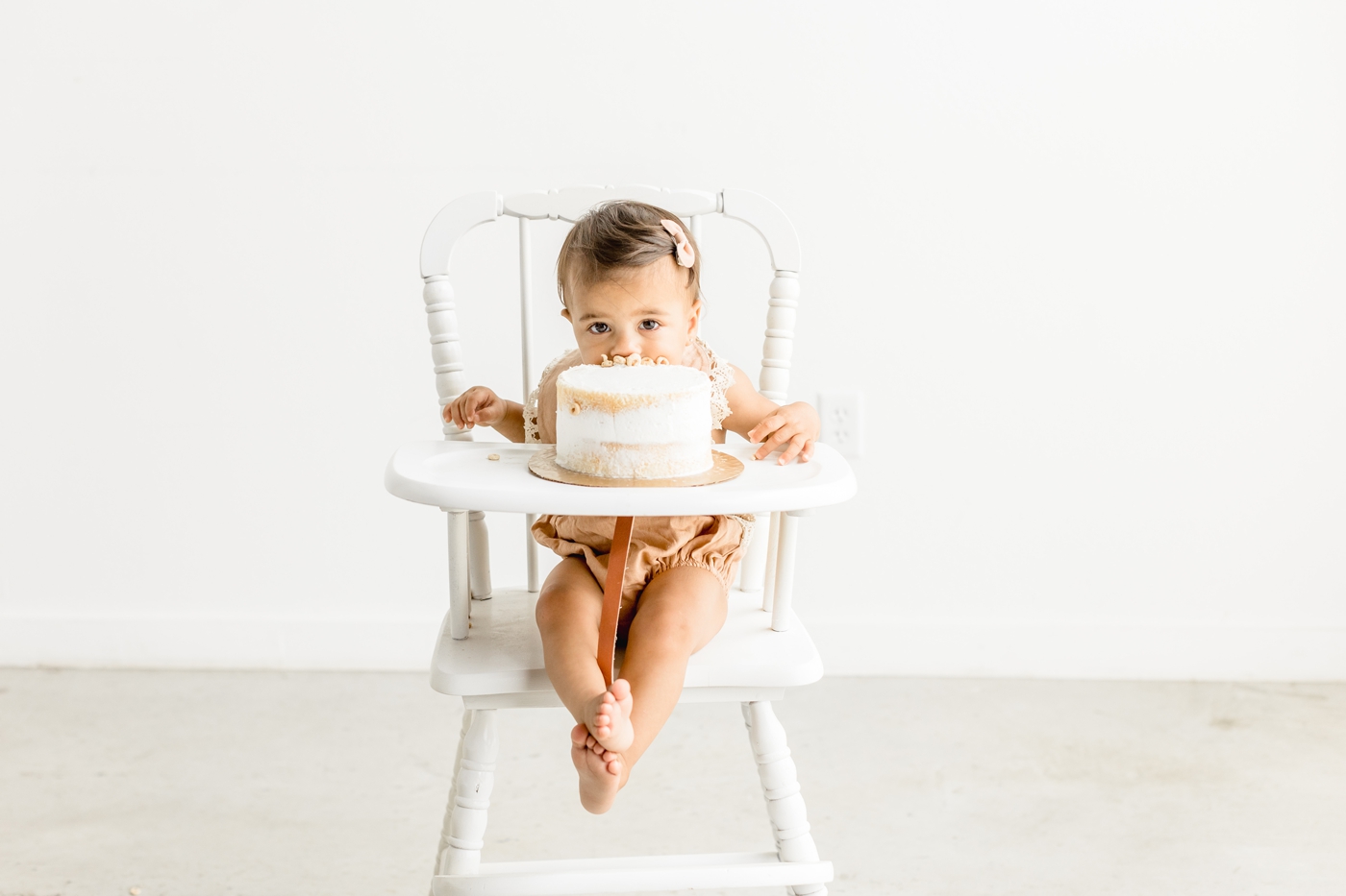 Little girl biting cake during first birthday cake smash with Sana Ahmed Photography.