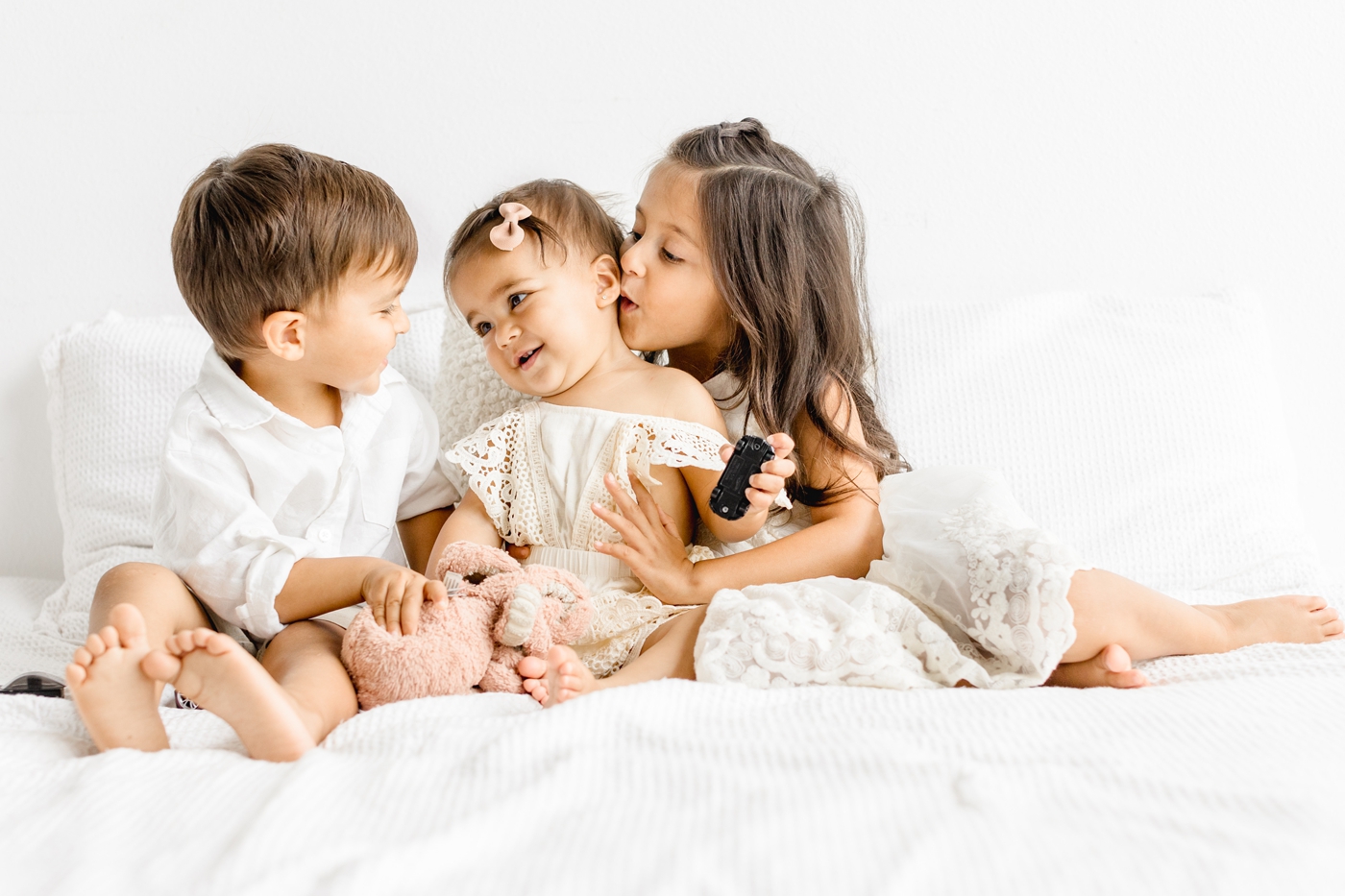 Sweet sibling image with three children sitting on studio bed. Photo by Austin family photographer, Sana Ahmed Photography.