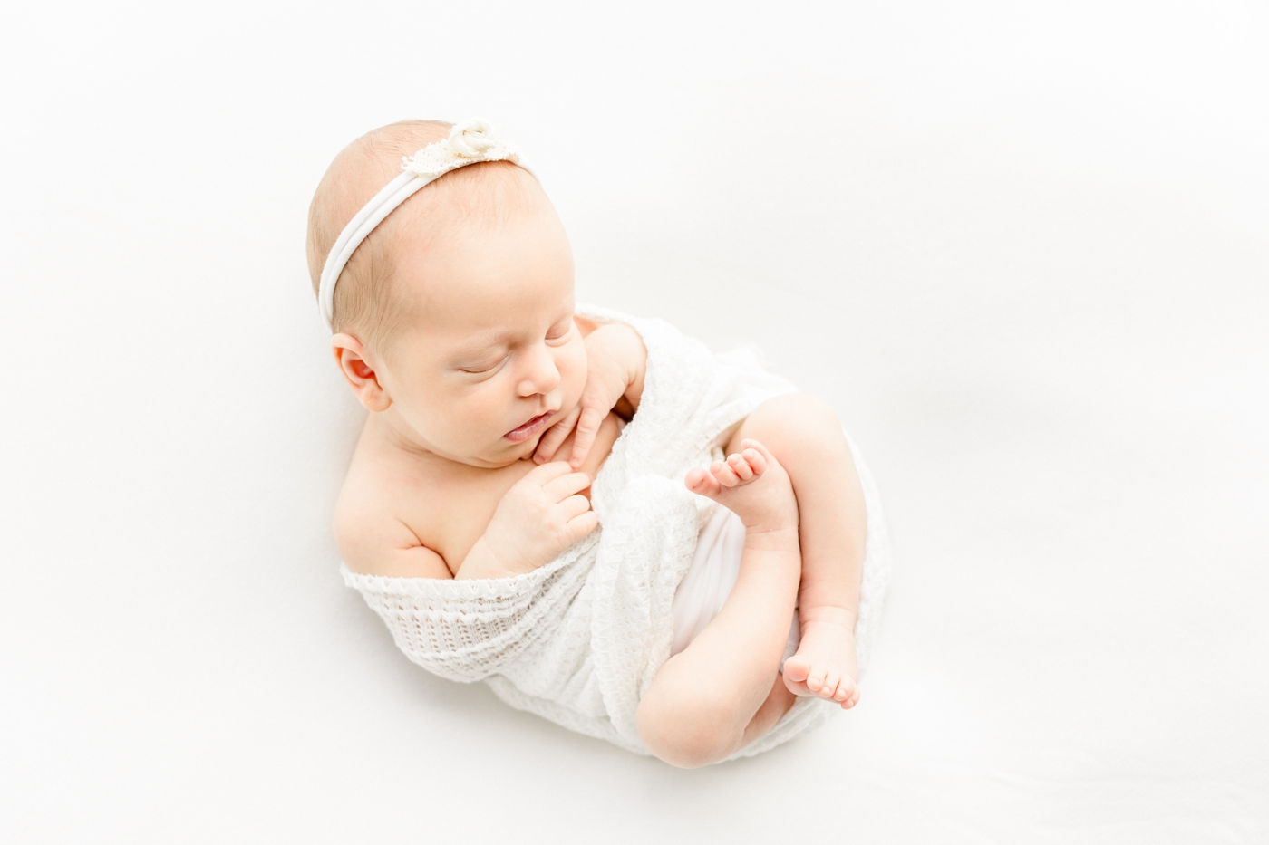 Sleeping baby in white knit swaddle during posed newborn session. Photo by Sana Ahmed Photography.