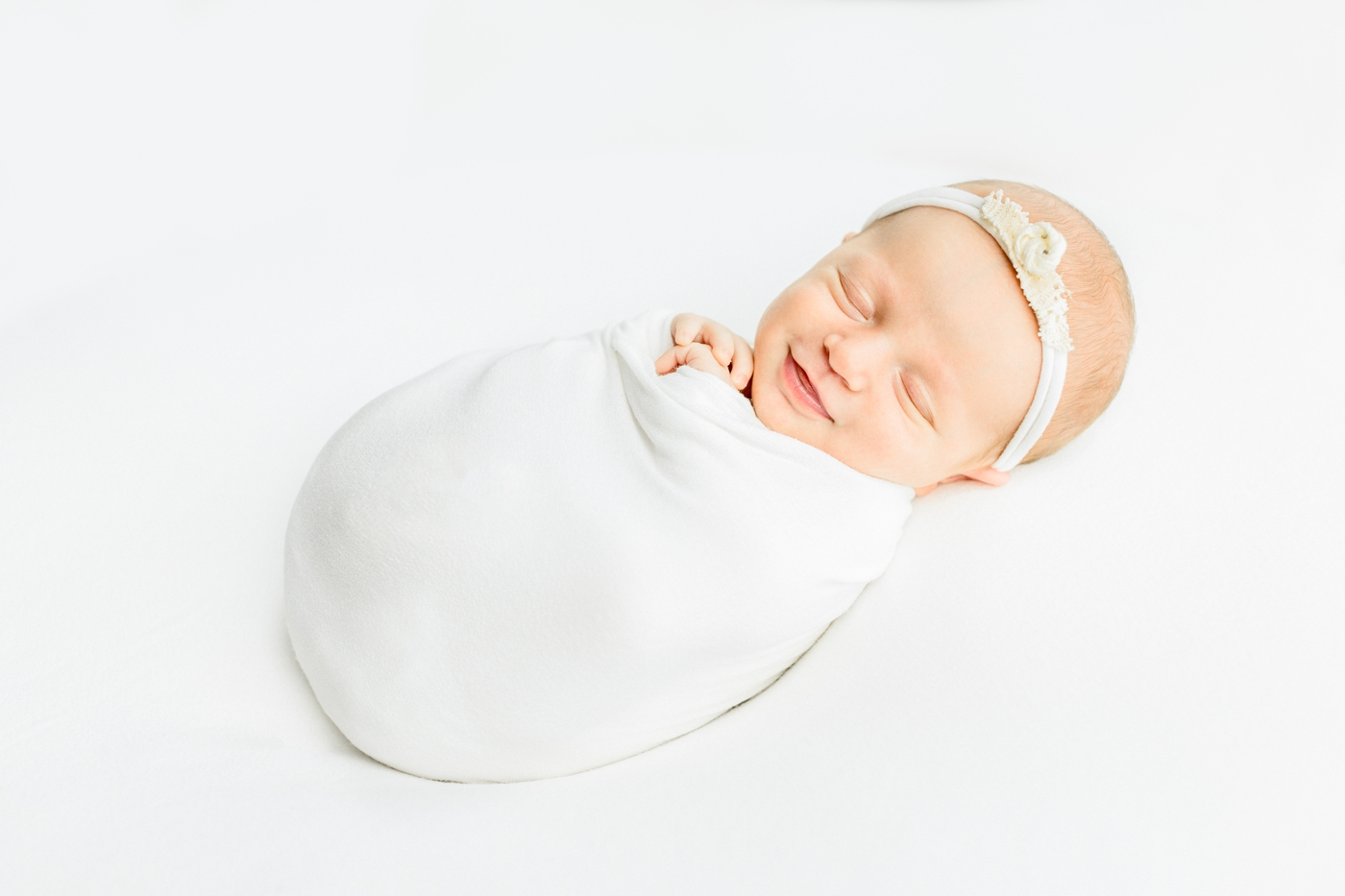 Baby girl in white swaddle smiling during her newborn photography session in Austin, TX studio with Sana Ahmed Photography.