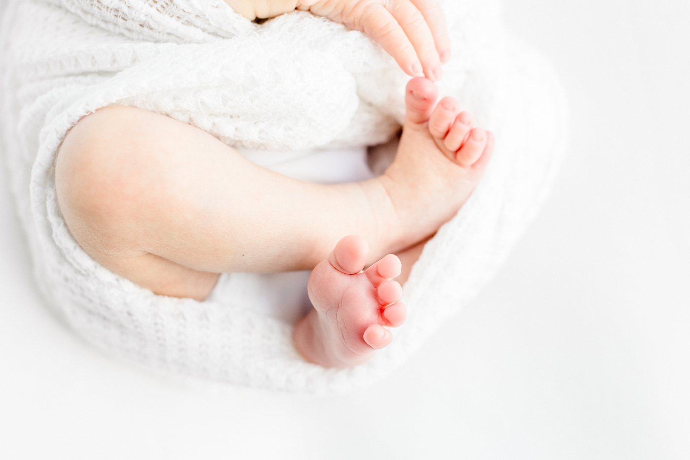 Closeup of newborn toes while baby is wrapped in white knit swaddle. Photo by Sana Ahmed Photography.