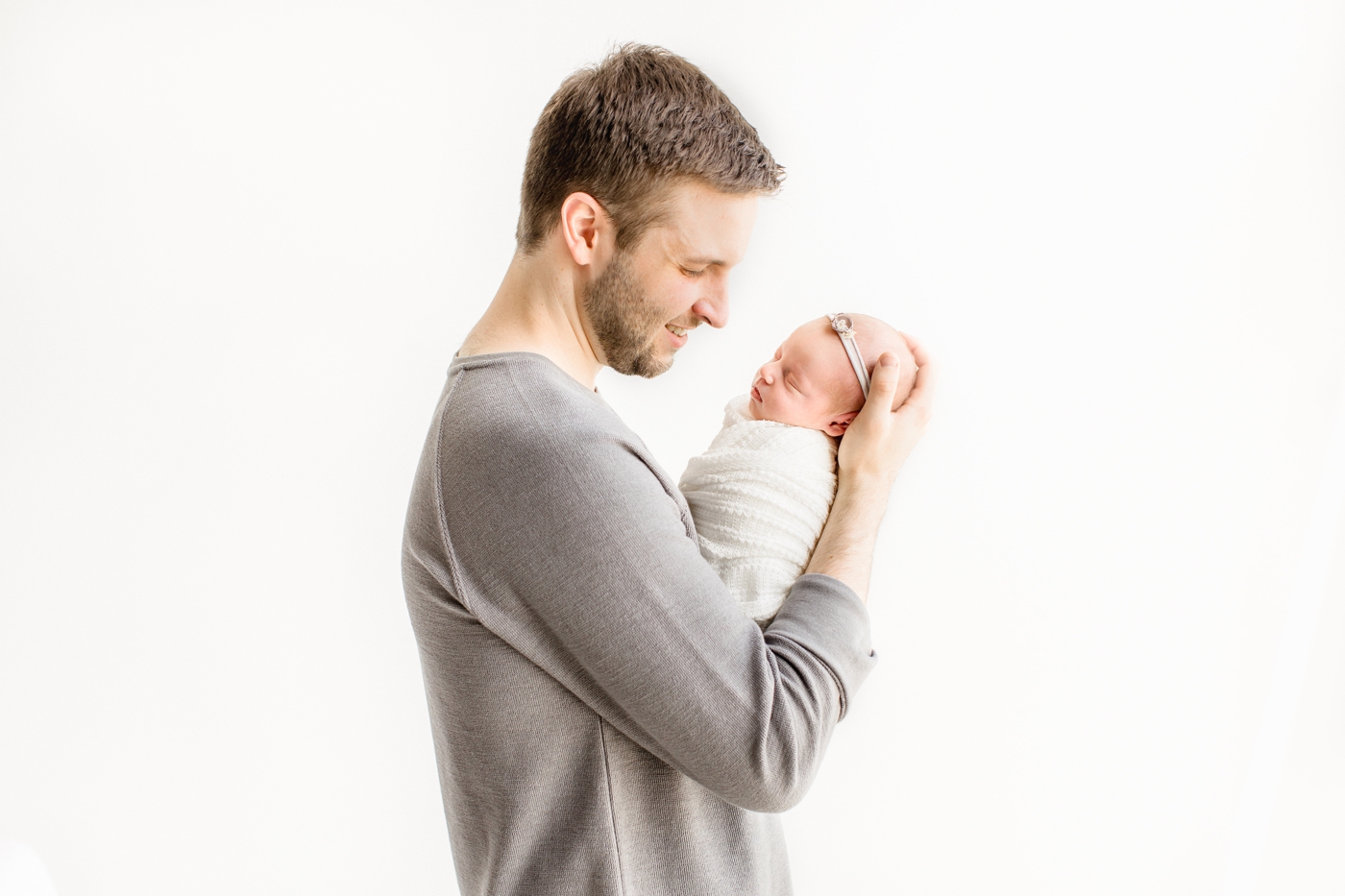 Dad holding baby in his arms and looking down at her. Photo by Austin newborn photographer, Sana Ahmed Photography.