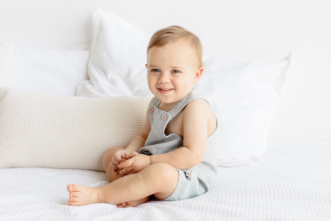 Toddler boy smiling at camera on bed. Photo by Sana Ahmed Photography.