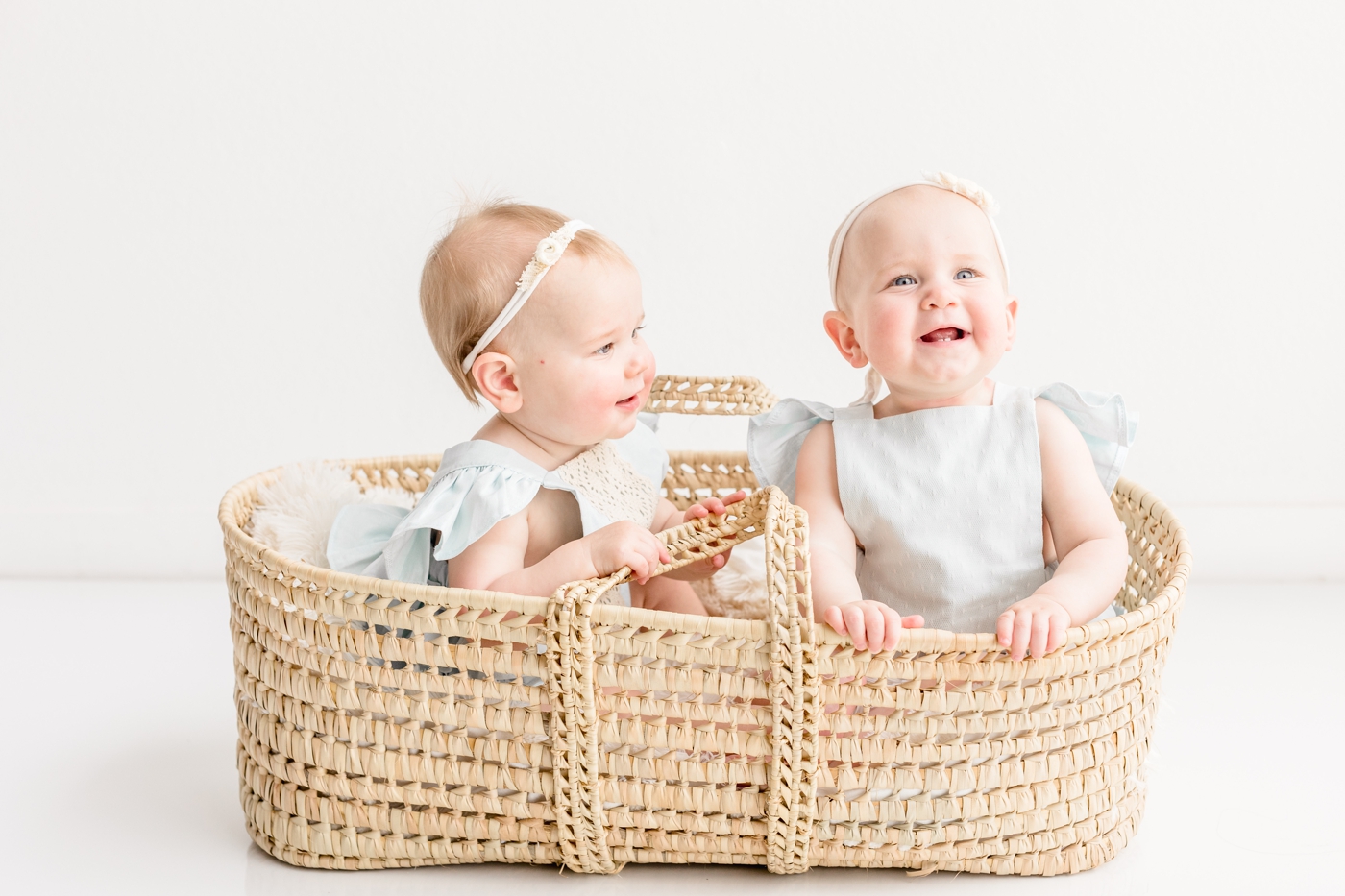 Smiling twins as they sit in moses basket during first birthday photo session with Sana Ahmed Photography.