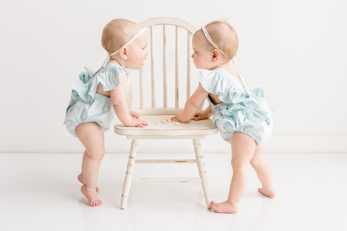 Twin girls in blue rompers standing together in studio. Photo by Sana Ahmed Photography.