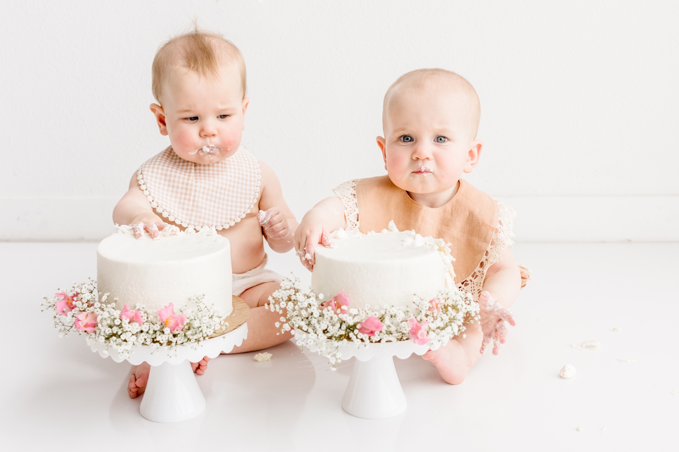 Twins digging into cake during first birthday milestone session in studio. Photo by Sana Ahmed Photography.
