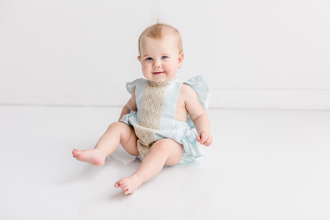 Smiling baby girl in blue bubble romper during first birthday milestone session. Photo by Sana Ahmed Photography.