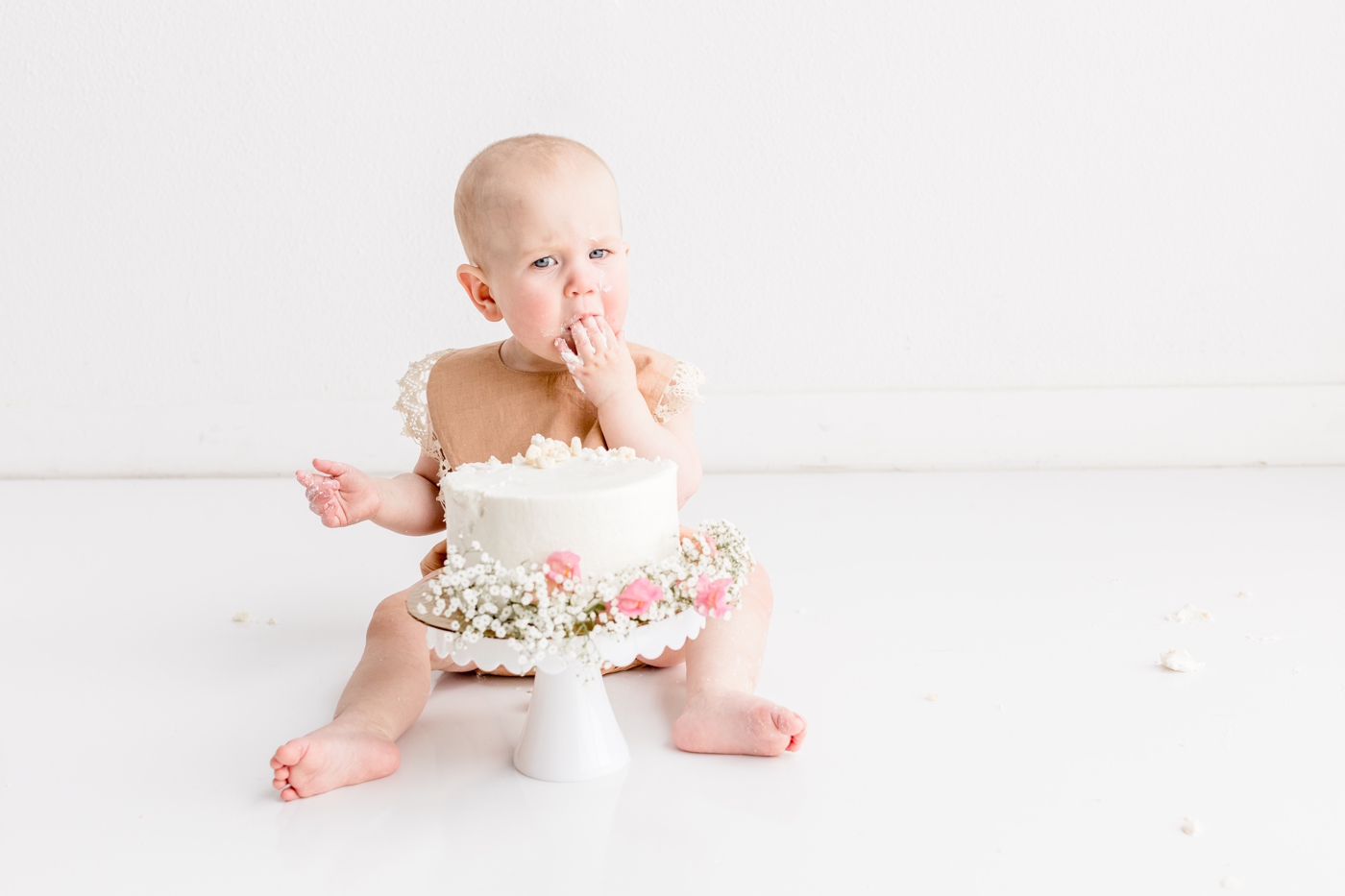 Twin girl getting first taste of frosting during cake smash session in Austin TX. Photo by Sana Ahmed Photography.