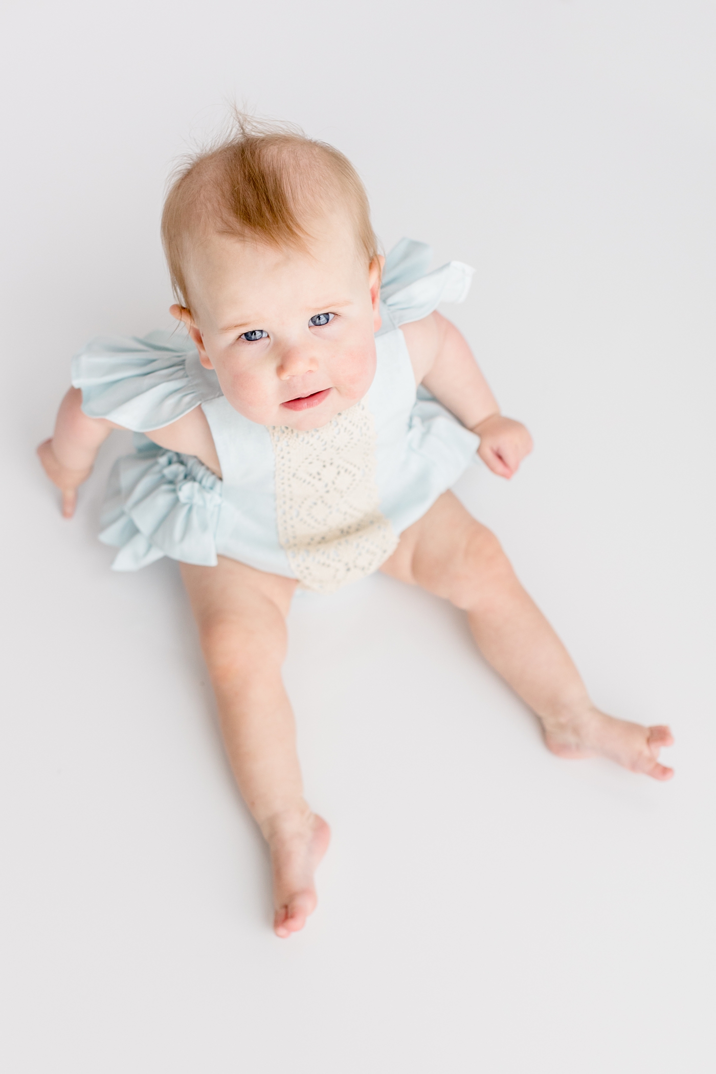 Blue eyed baby girl looking up at camera during photo session. Image by Sana Ahmed Photography.