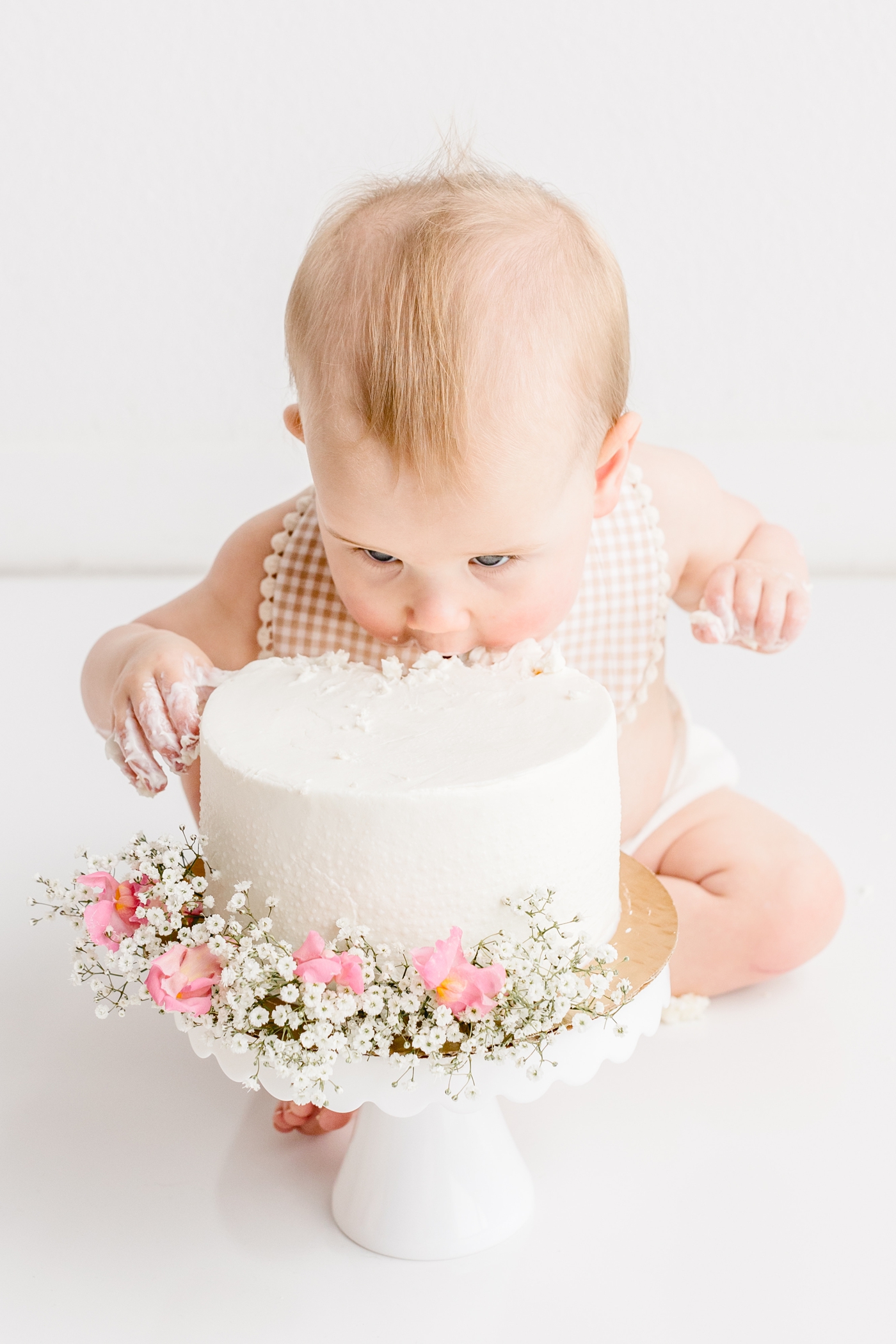 Baby girl taking a bite of her cake with florals on it during first birthday photo session. Photo by Sana Ahmed Photography.