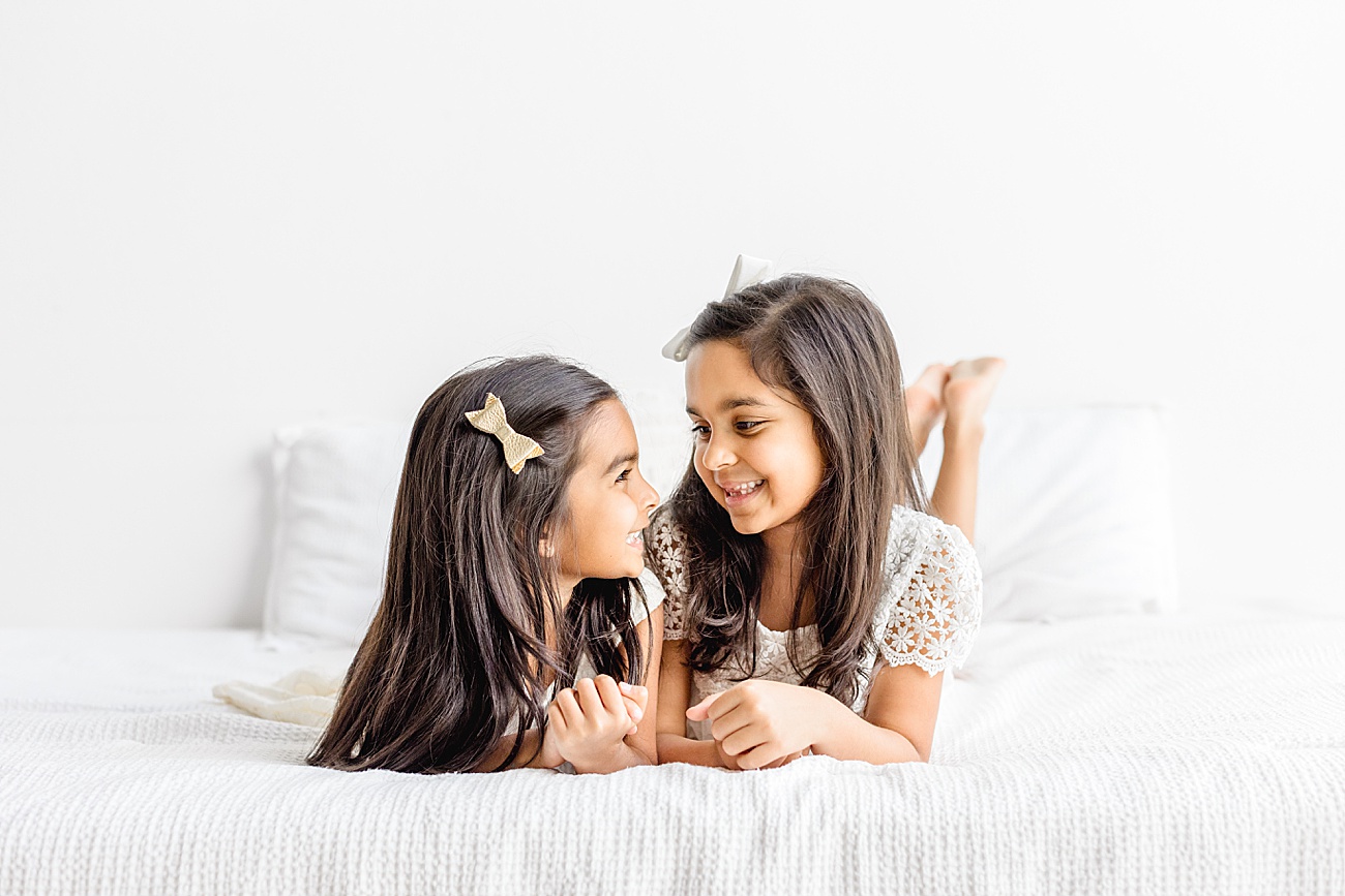 Adorable portrait of sisters looking at each other during family session in Austin studio. Photo by Sana Ahmed Photography.