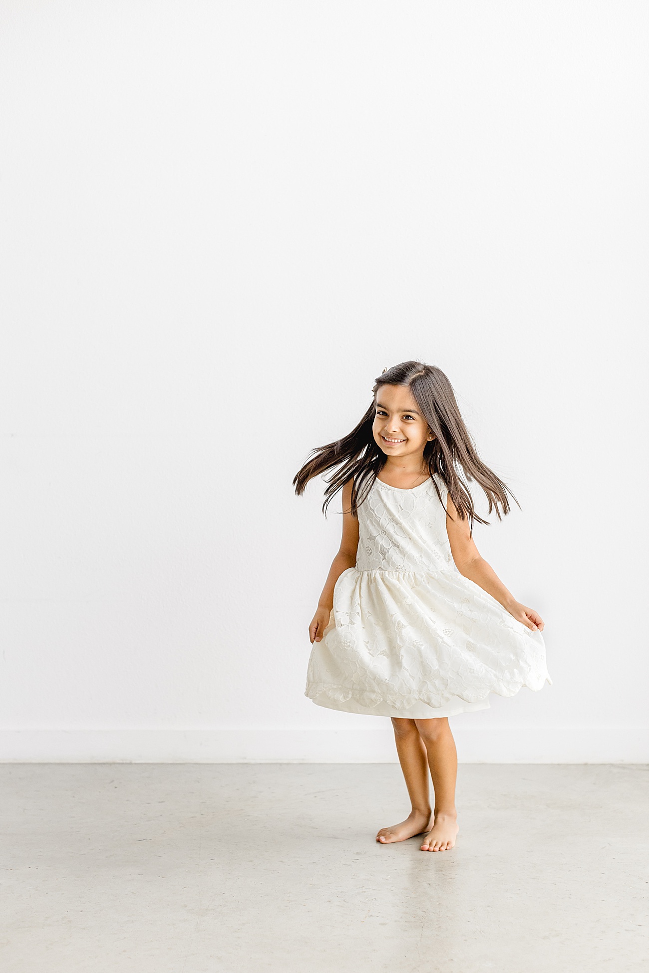Little girl twirling in white dress in studio. Photo by Sana Ahmed Photography.
