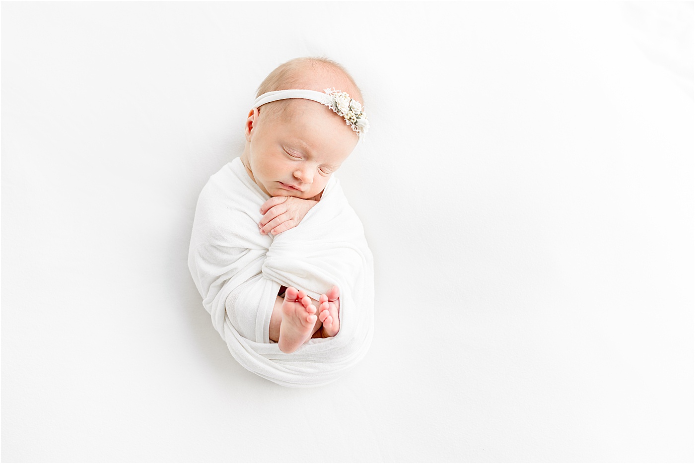 Wide angle photo of baby girl in white swaddle sleeping during newborn photos. Photo by Sana Ahmed Photography.