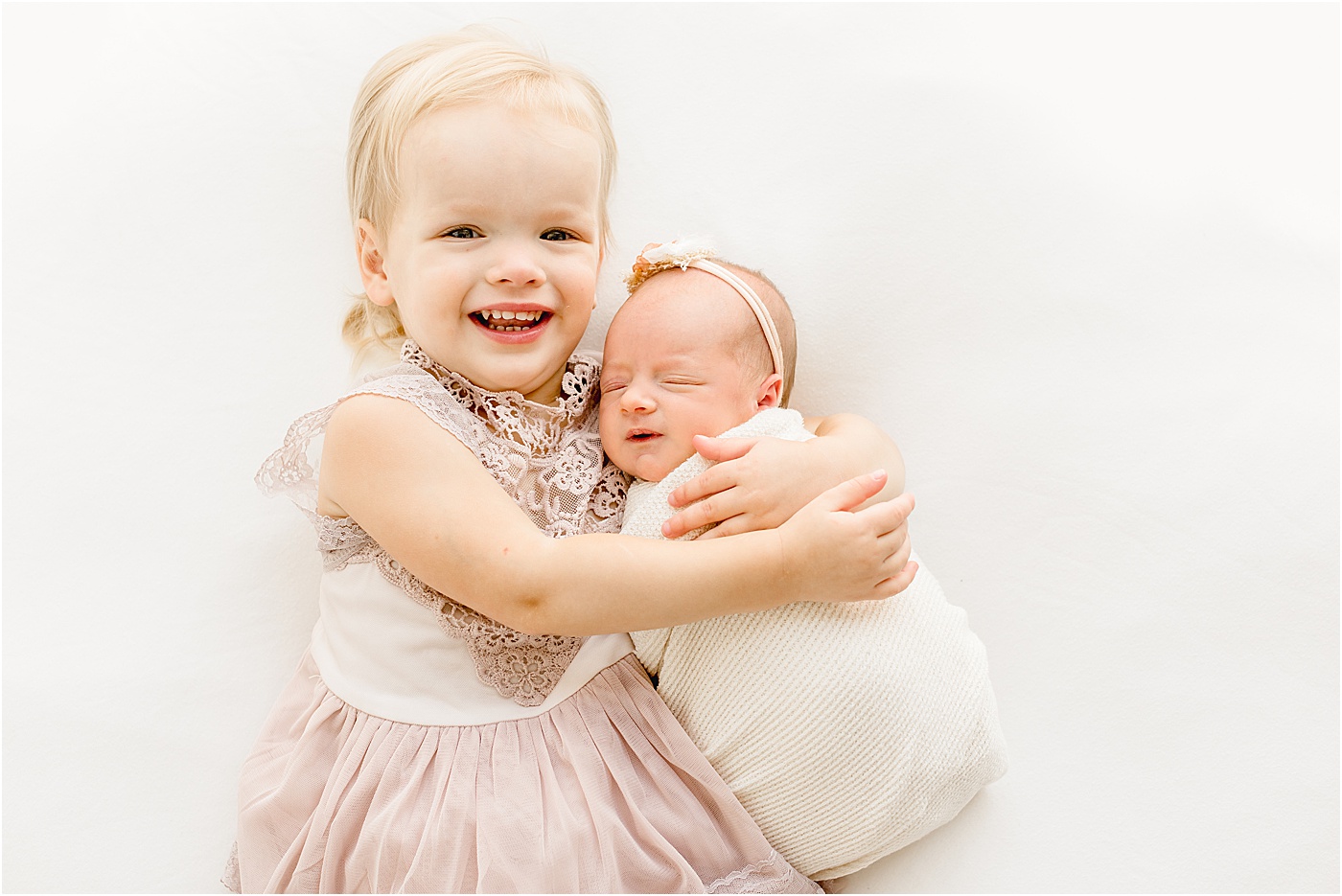 Sweet sibling moment as big sister holds baby sister during newborn photography session in Austin.