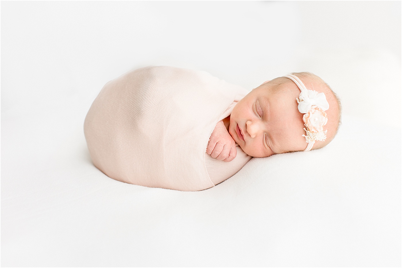 Sleeping baby in blush pink swaddle on white background. Photo by Sana Ahmed Photography.
