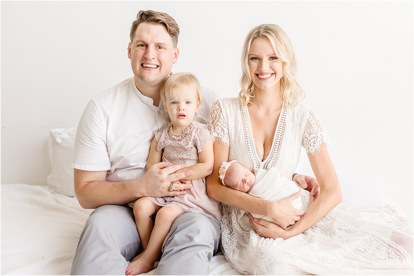 Sweet family portrait with 2 year old and newborn as they sit on studio bed in Austin, TX. Photo by Sana Ahmed Photography.