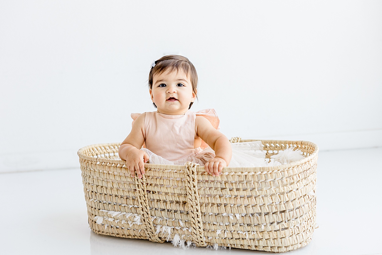 Baby smiling while she sits in moses basket. Photo by Sana Ahmed Photography