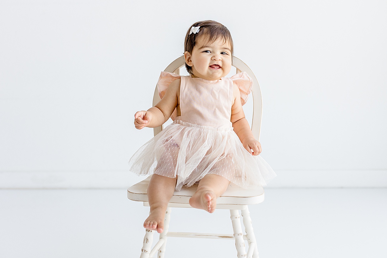 Photo of baby sitting on white wooden chair during studio milestone session with Sana Ahmed Photography.