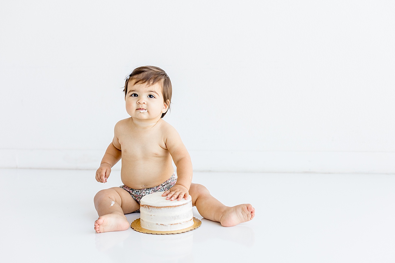 Photo of baby touching cake during one year birthday session. Photo by Sana Ahmed Photography