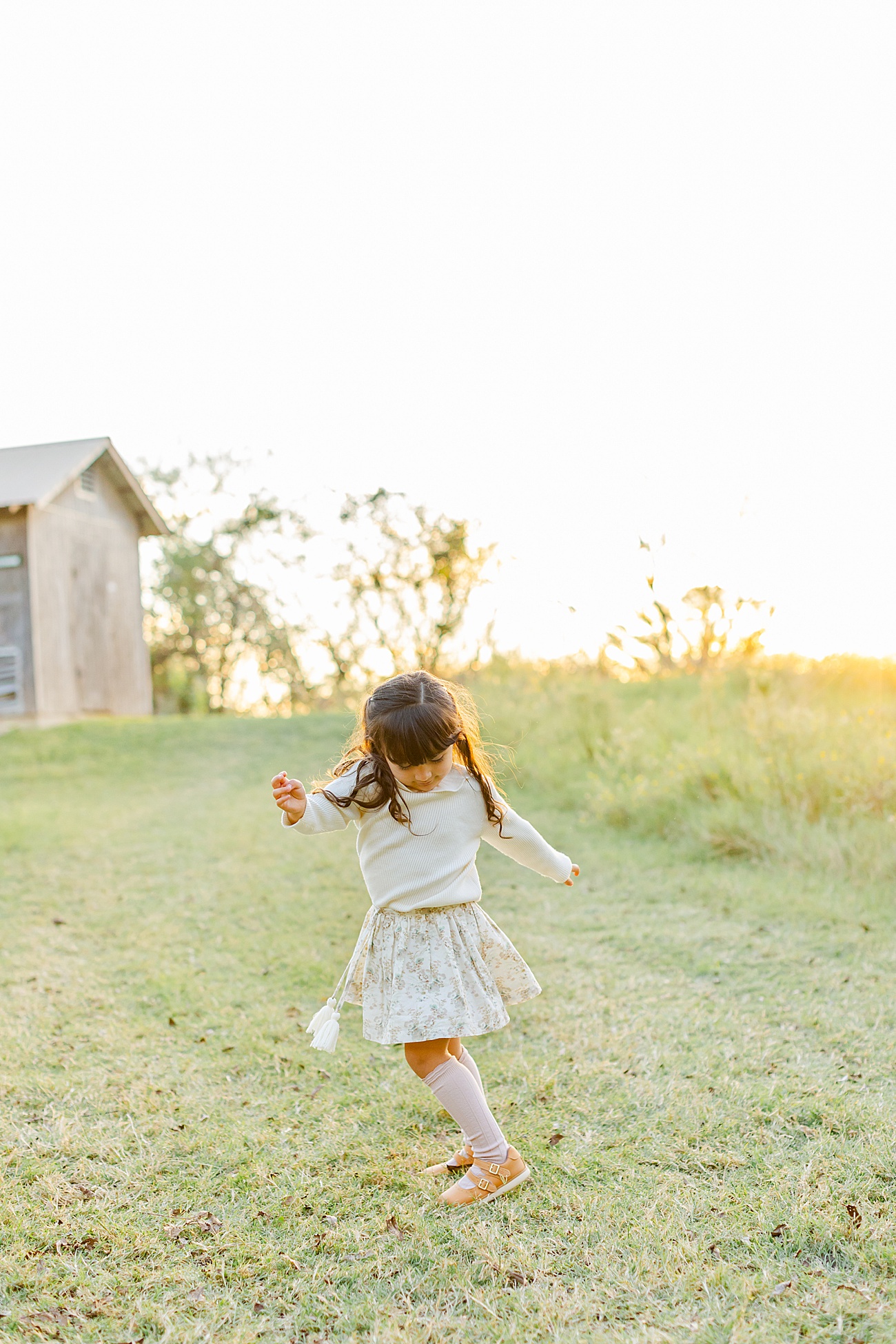 Toddler girl spinning in sun-drenched field during family session near Round Rock, TX, Photo by Sana Ahmed Photography