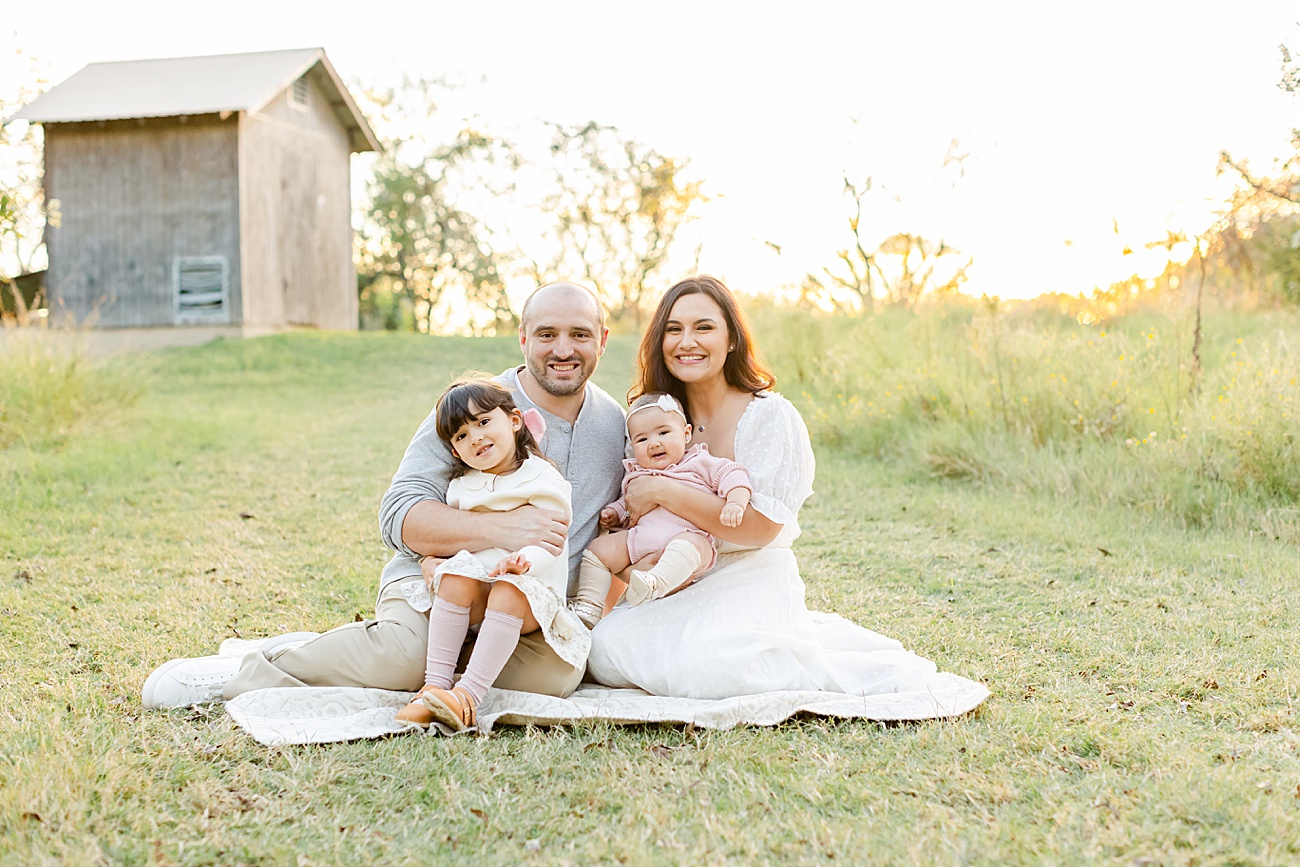 Family smiling at camera as they sit on a blanket in field near Round Rock, TX. Photo by Sana Ahmed Photography