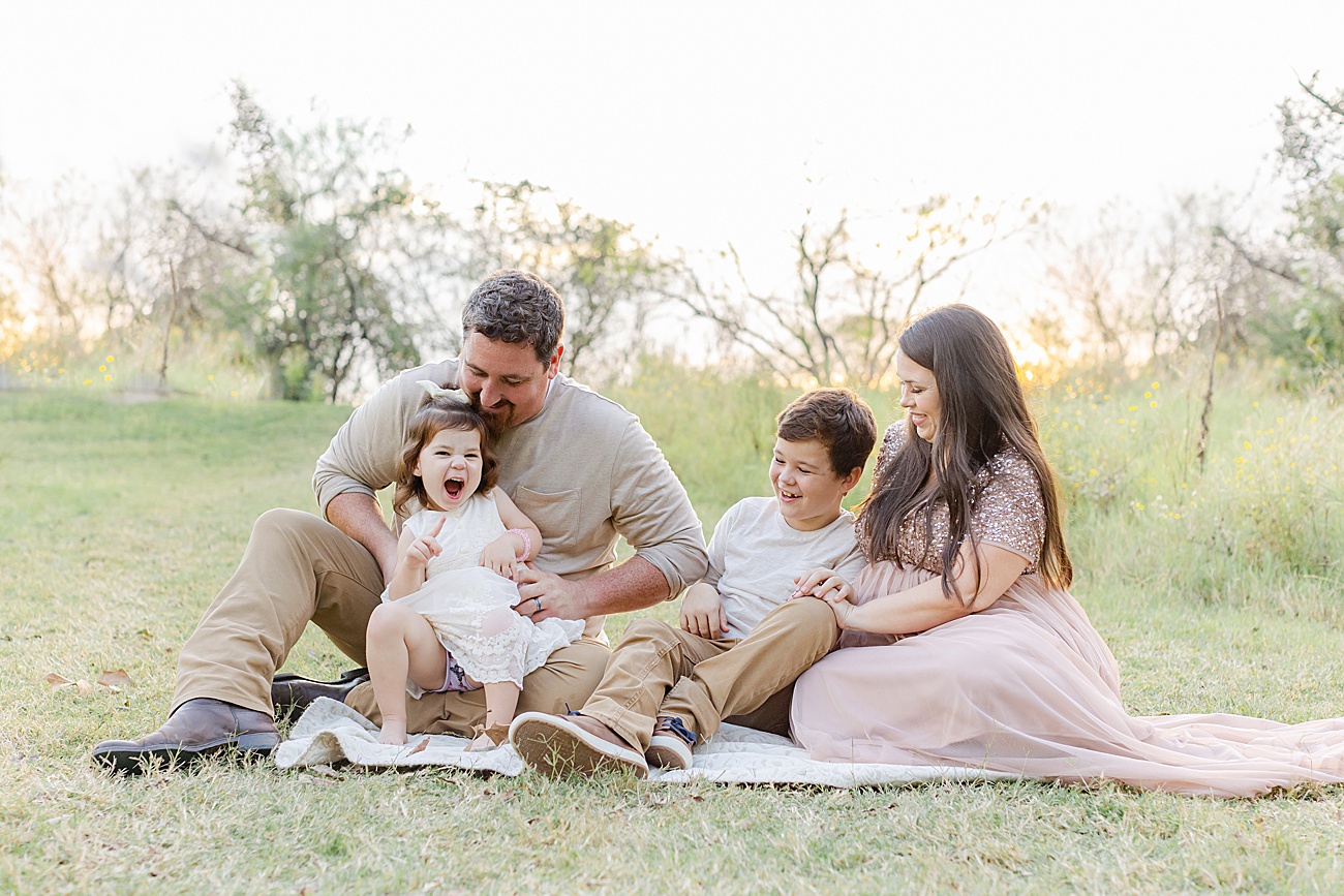 Family cuddling on blanket in sunlit field during maternity session with Sana Ahmed Photography