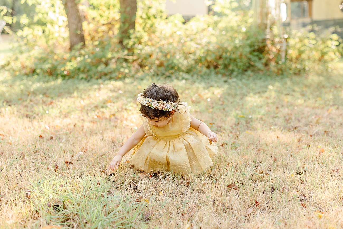 Little girl bending down in field with sun coming through the trees behind her in Austin, TX. Photo by Sana Ahmed Photography