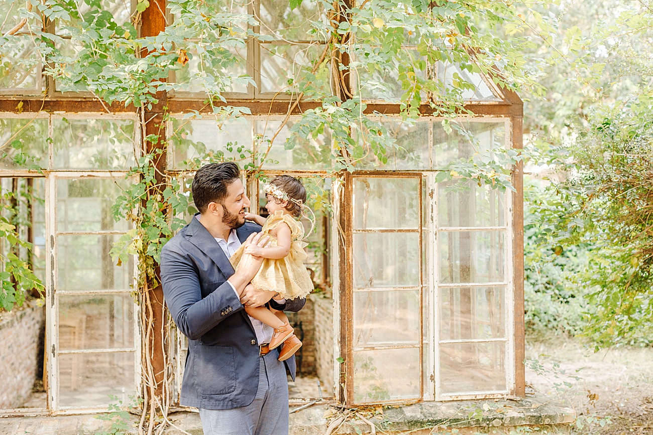 Dad holding little girl outside of vintage greenhouse. Photo by Sana Ahmed Photography