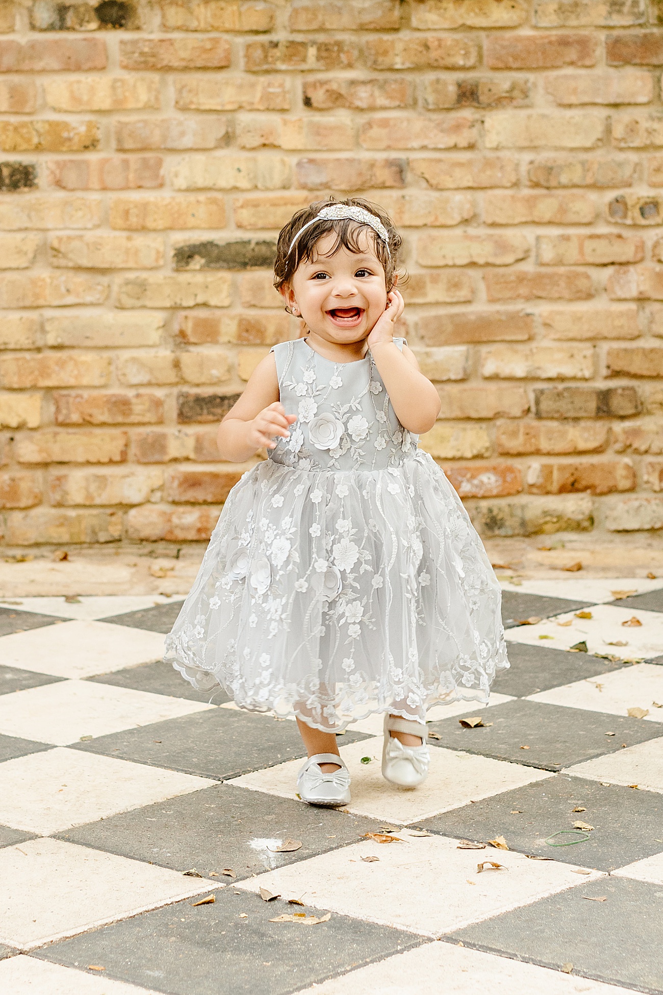 Smiling little girl wearing grey floral dress during first birthday photo session.Photo by Sana Ahmed Photography