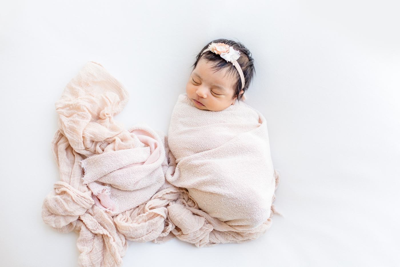 Beautiful baby girl in blush swaddle and small bow during newborn session with Sana Ahmed Photography.
