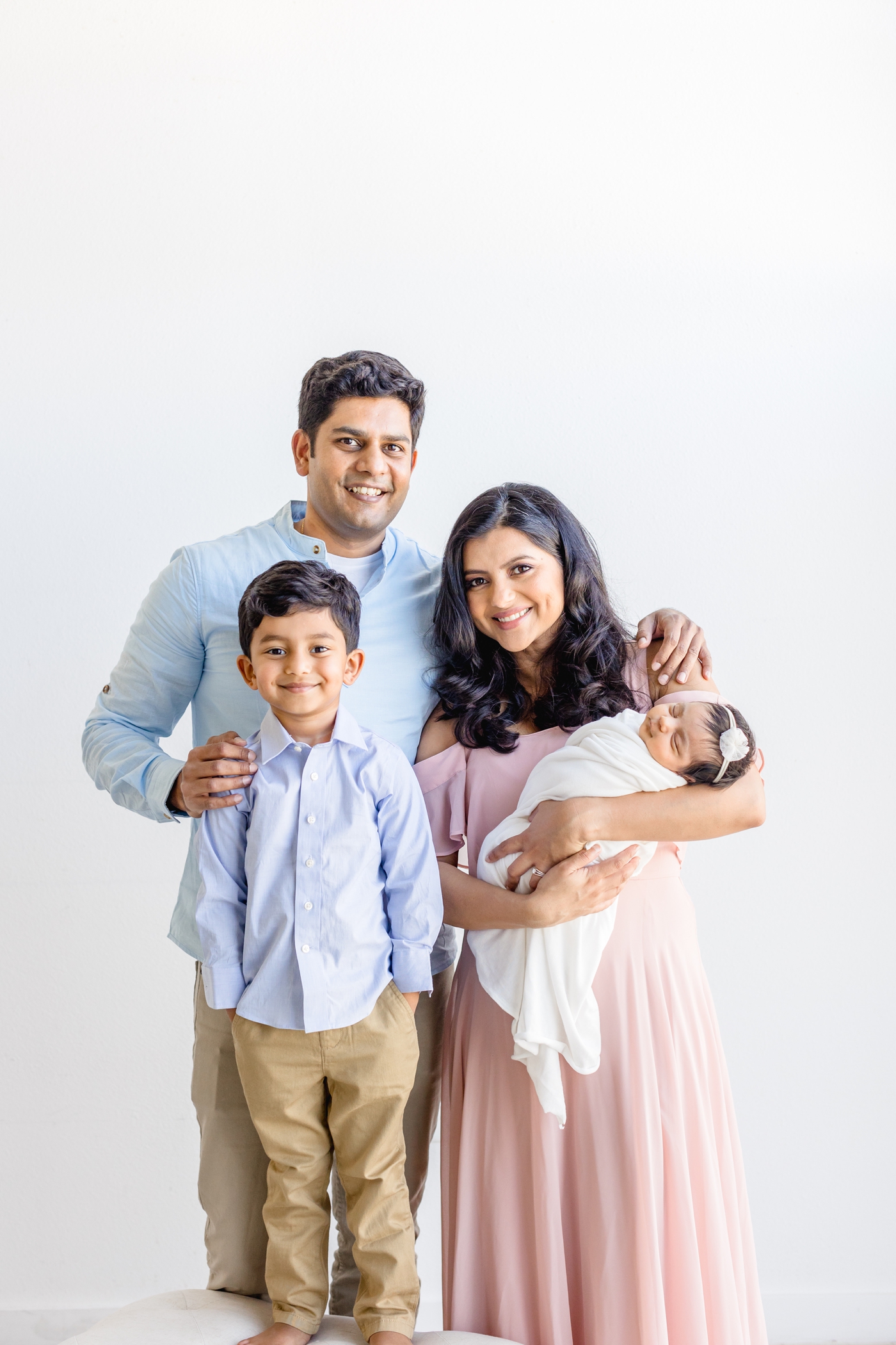 Family of four smiling at camera during studio newborn session with Sana Ahmed Photography.
