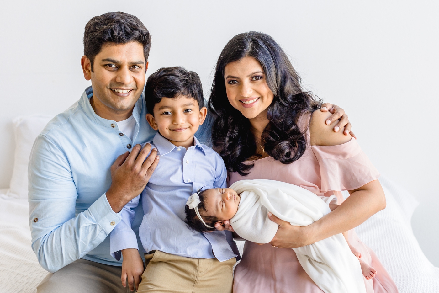 Sweet image of family of four smiling at the camera during newborn session with video. Image by Sana Ahmed Photography.