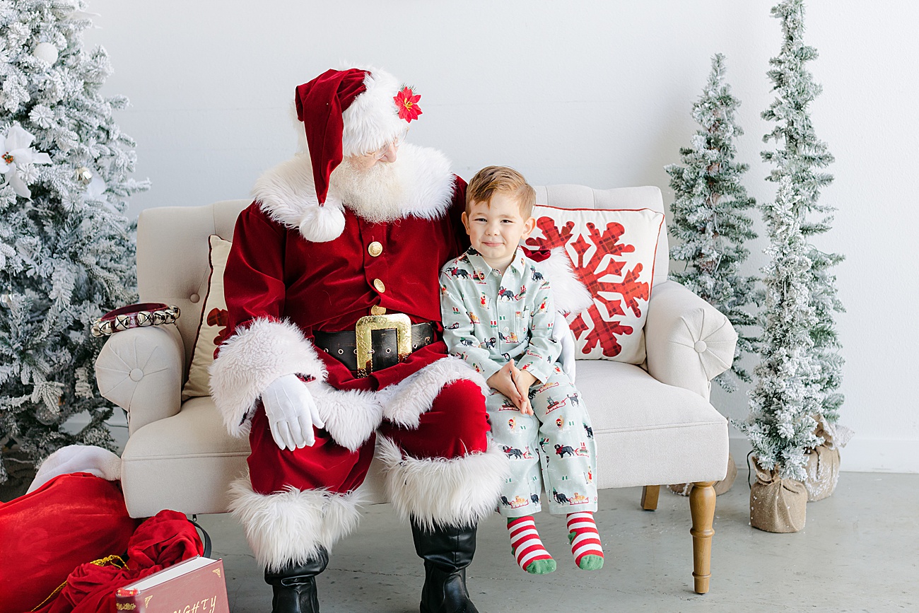 Happy boy sitting next to Santa during mini session event with Sana Ahmed Photography.