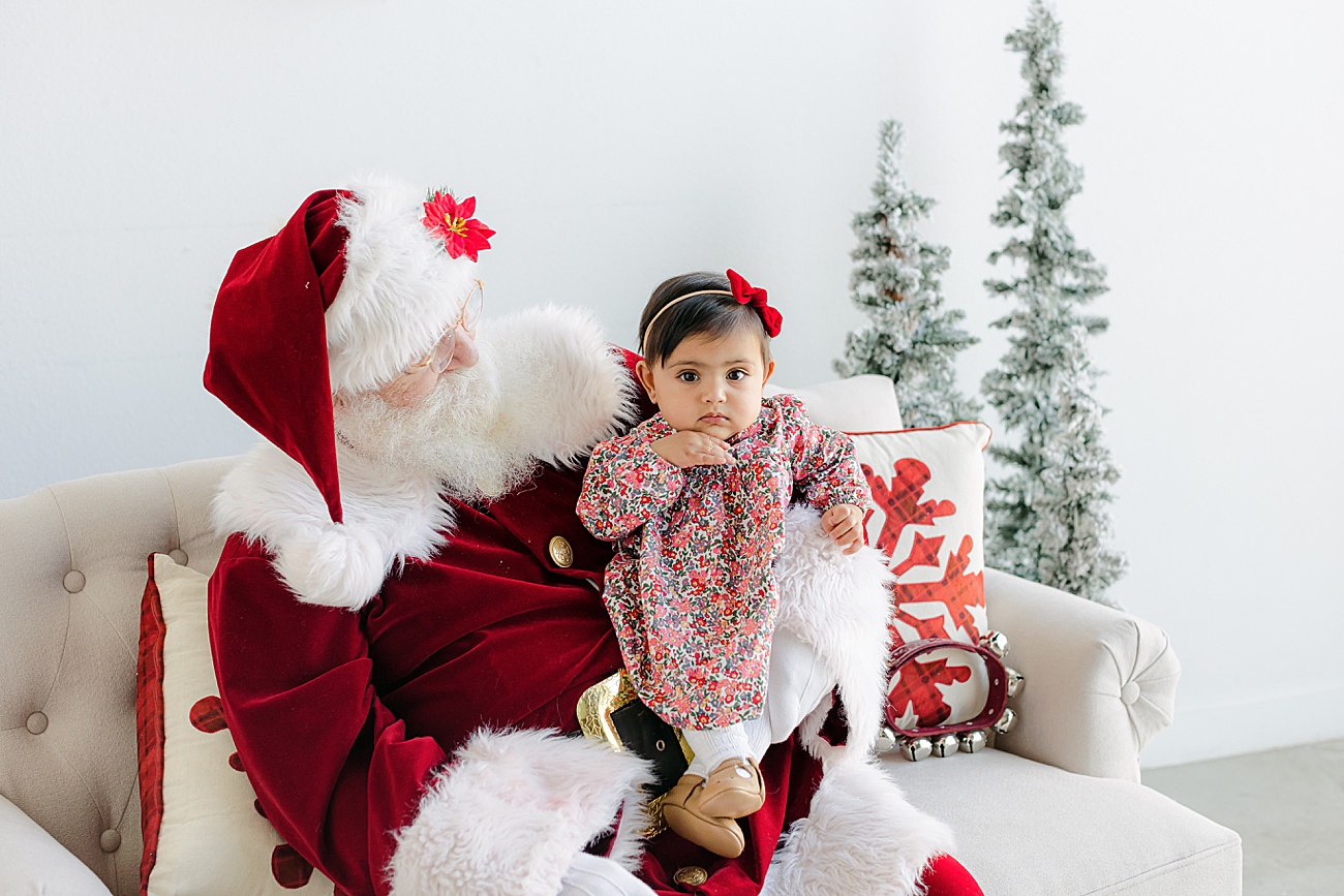 Serious baby girl sitting on Santa's lap. Photo by Sana Ahmed Photography.