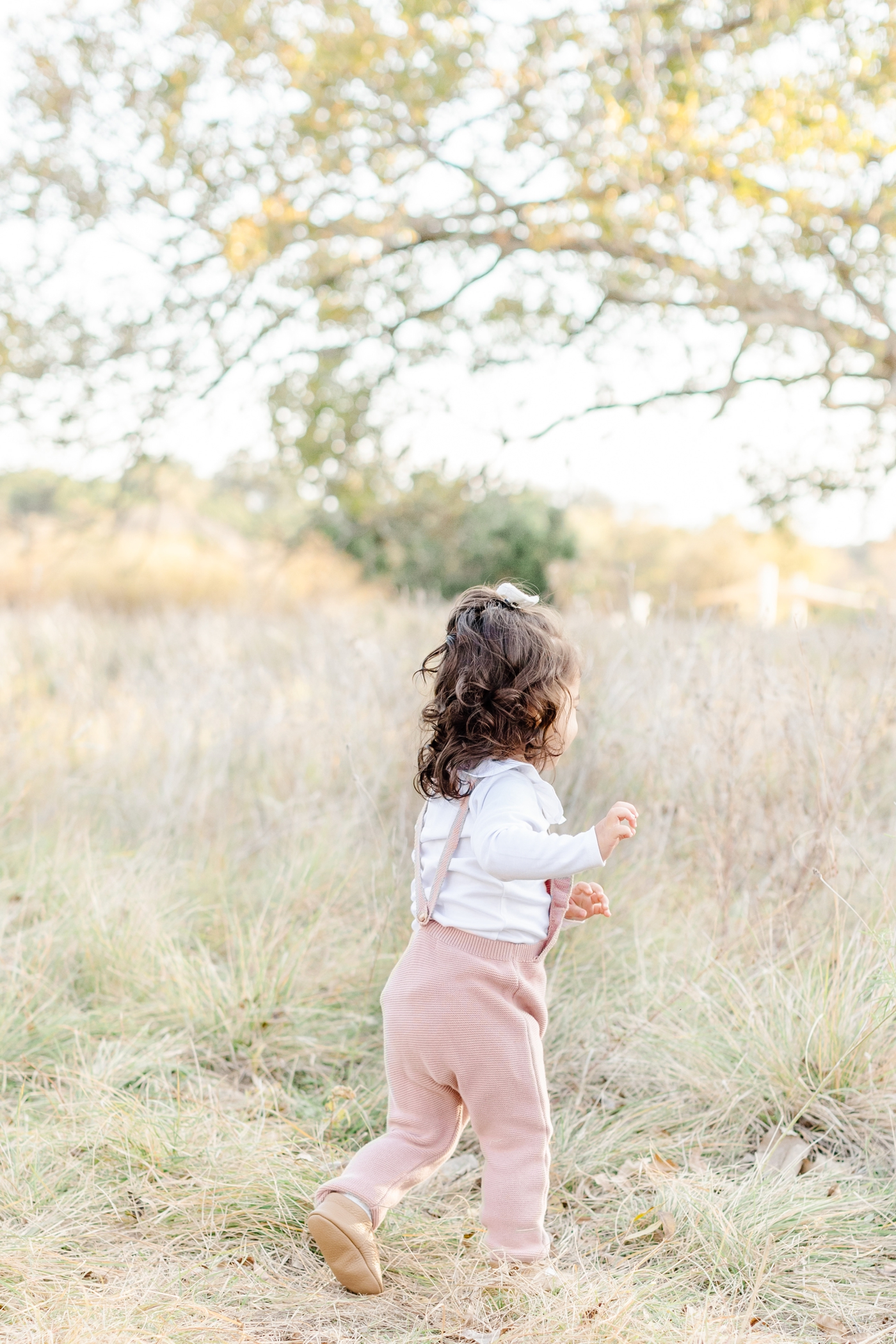 Toddler wearing pink knit jumpsuit playing in field with tall grass. Photo by Austin family photographer, Sana Ahmed Photography.