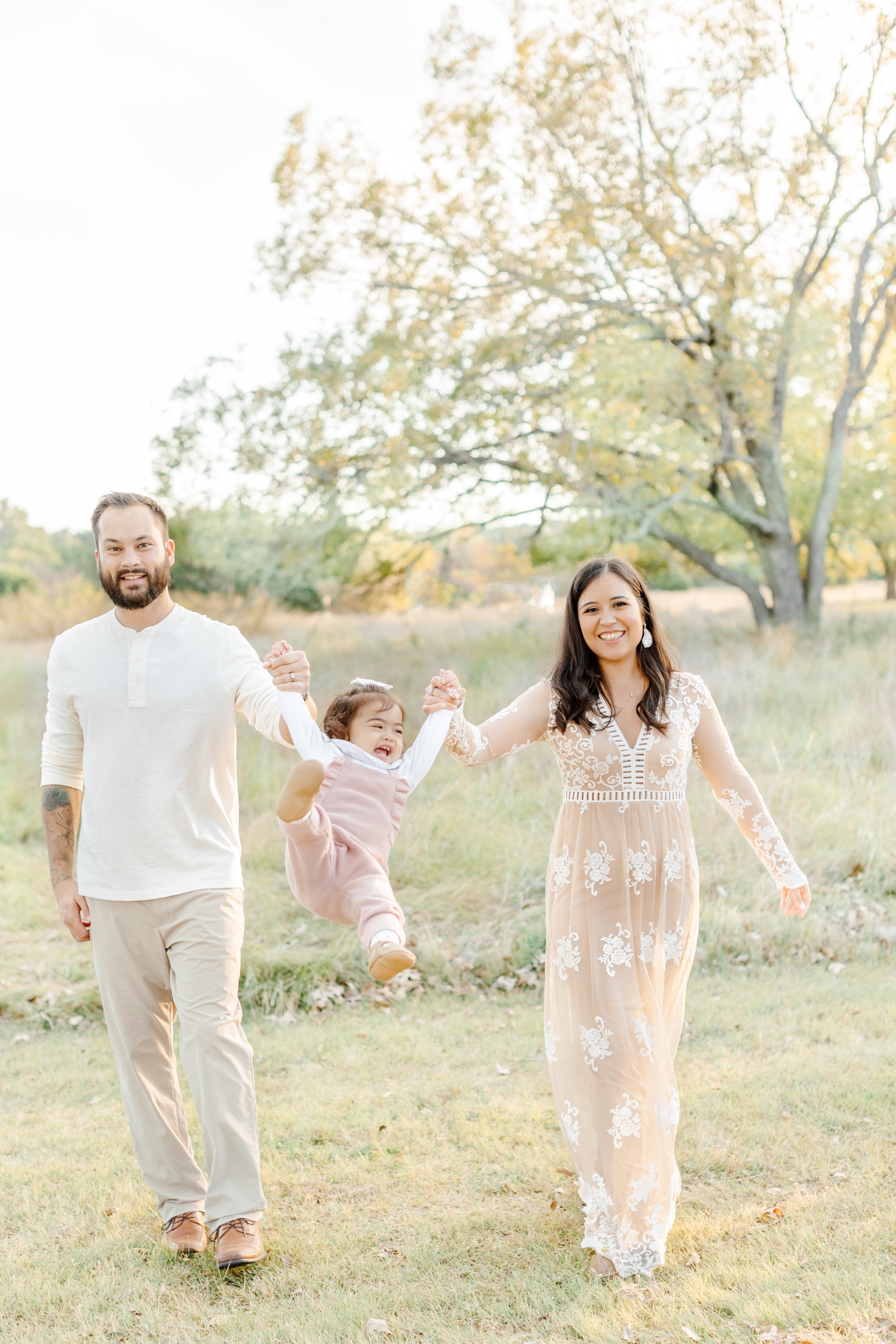 Playful image of parents swinging little girl as they walk in Austin, TX park during family session with by Sana Ahmed Photography.