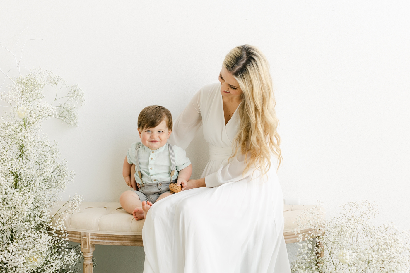 Mom sitting on bench with little boy, surrounded by baby's breath, during Motherhood portrait event in Austin, TX. Photo by Sana Ahmed Photography.