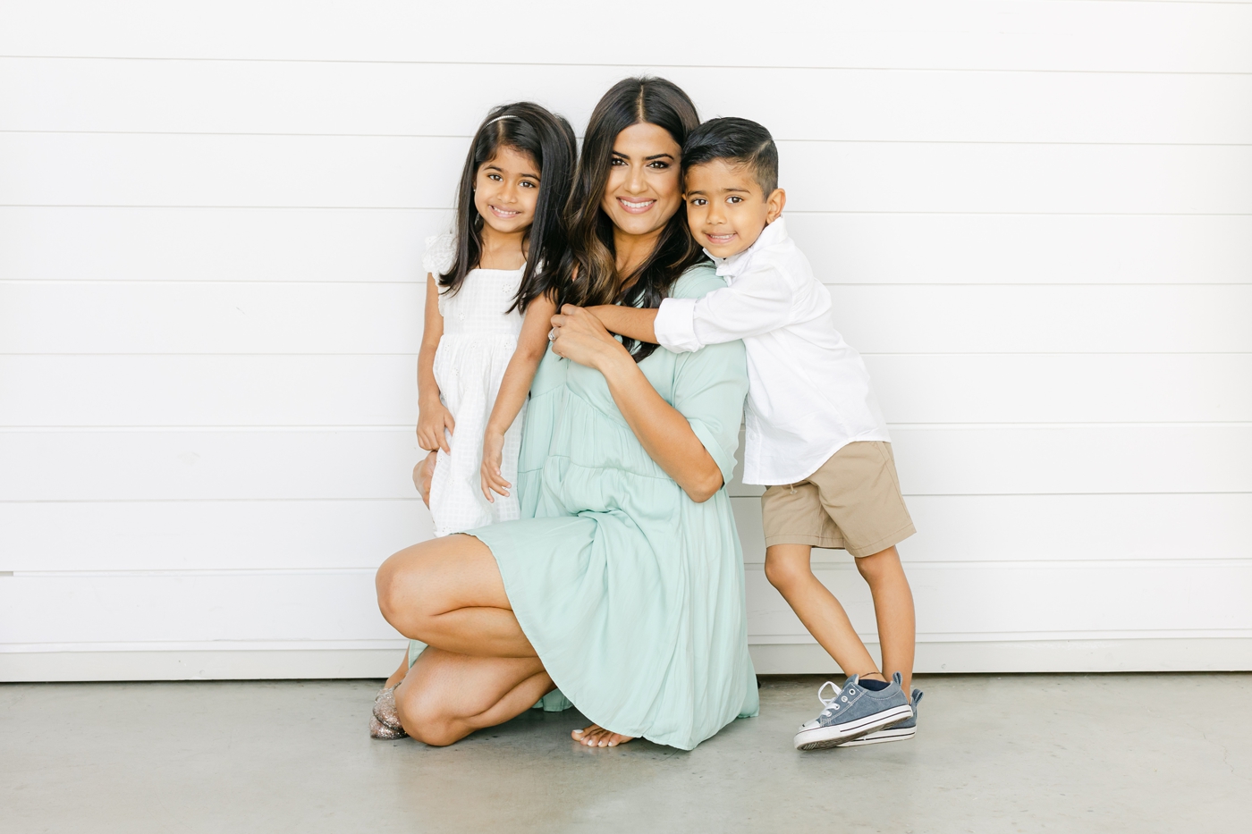 Mom kneeling with kids wrapped around her during motherhood mini session event. Photo by Sana Ahmed Photography.